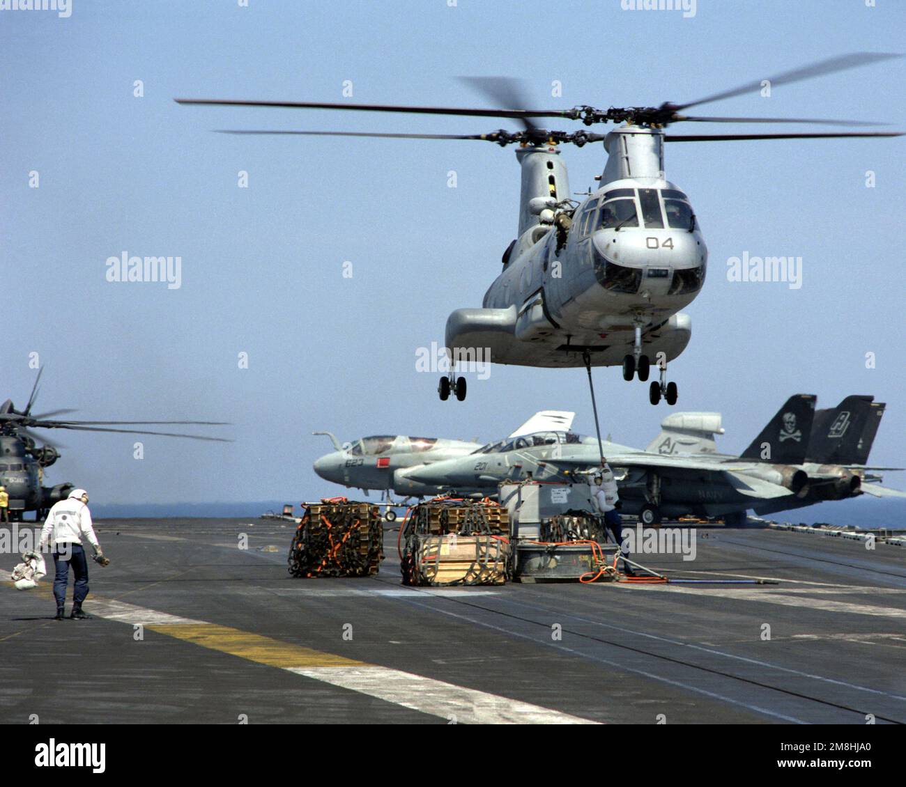 A flight deck crewman attaches a sling to the underside of an HH-46D ...