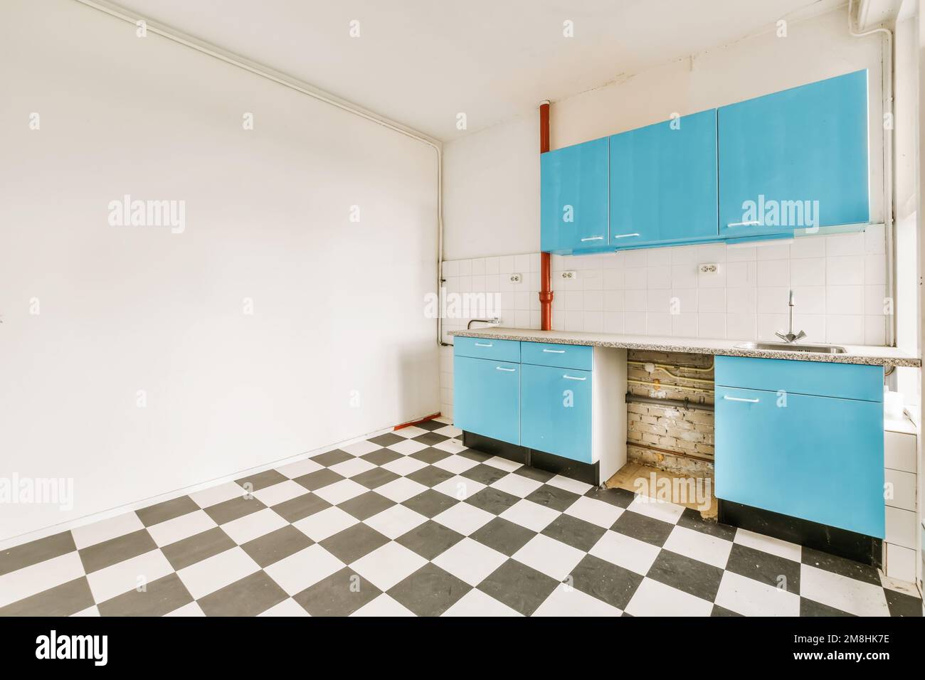 a kitchen with blue cabinets and black and white checkered flooring in an empty room that is being used for storage Stock Photo
