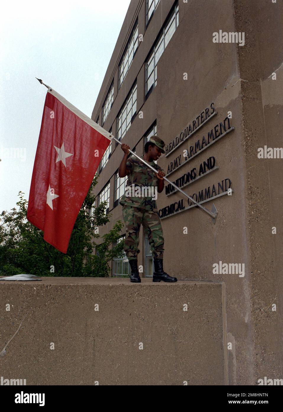 Sergeant Mark posts the commanding general's flag in front of the headquarters for the U.S. Army Armament Munitions and Chemical Command Building. Base: Rock Island State: Illinois (IL) Country: United States Of America (USA) Stock Photo