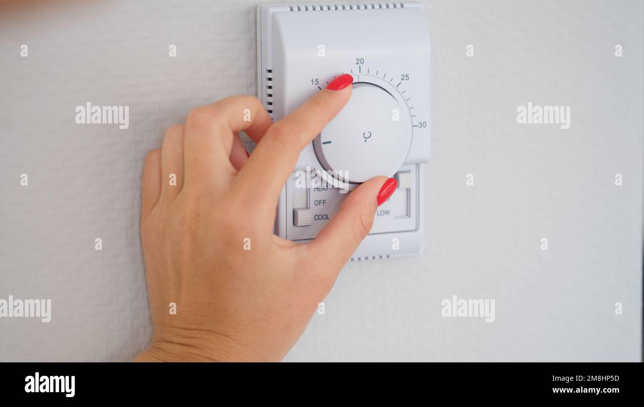 Woman hand adjusts or turns on wall temperature controller controller button Stock Photo