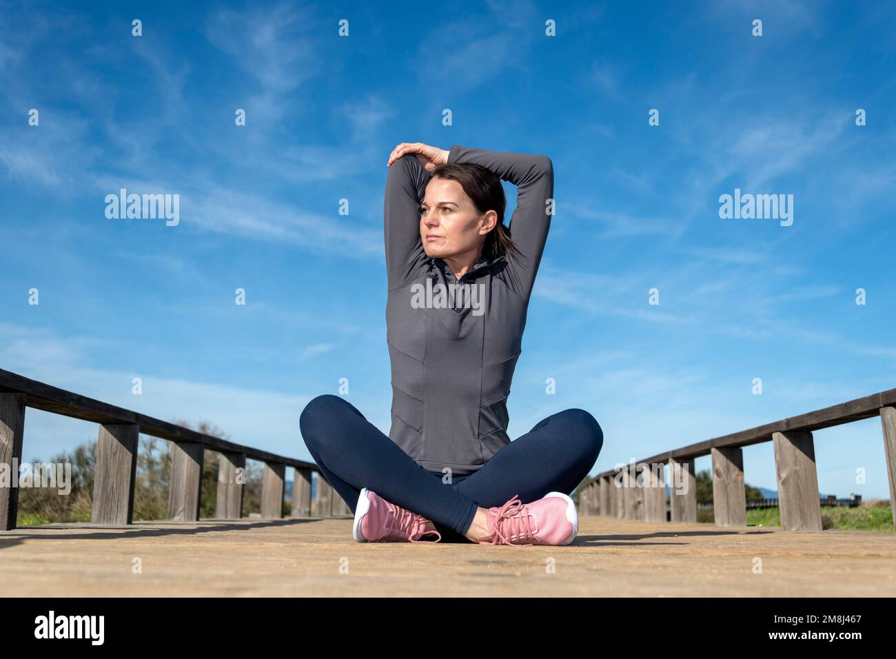 Sporty woman sitting cross legged doing an arm stretch warm up exercise. Stock Photo