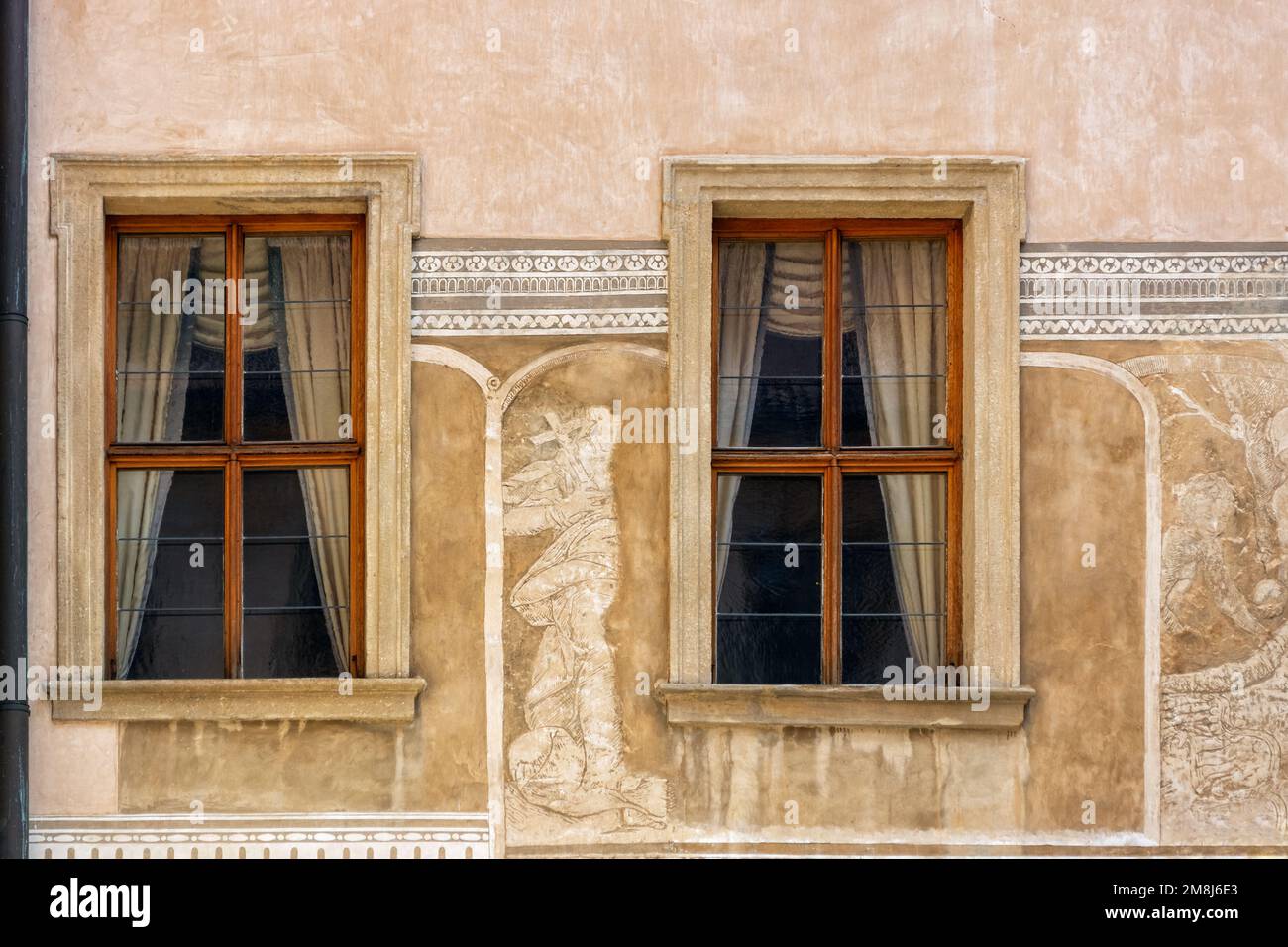 Two rectangular windows with brown wooden frames against a beige wall with an ancient bas-relief. From the Windows of the world series. Stock Photo