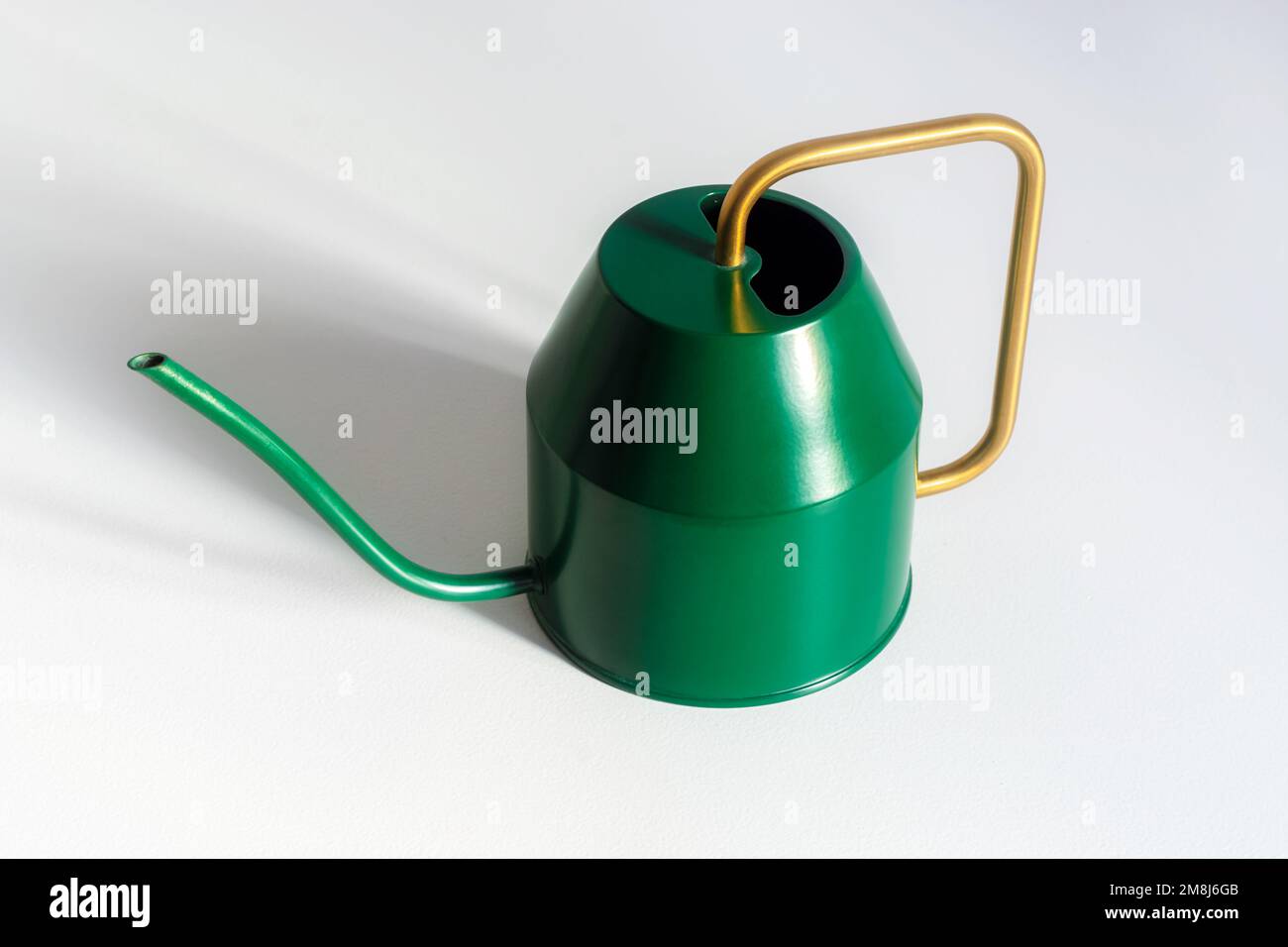Small decorative green watering can with a yellow handle for watering houseplants on a white background. Stock Photo