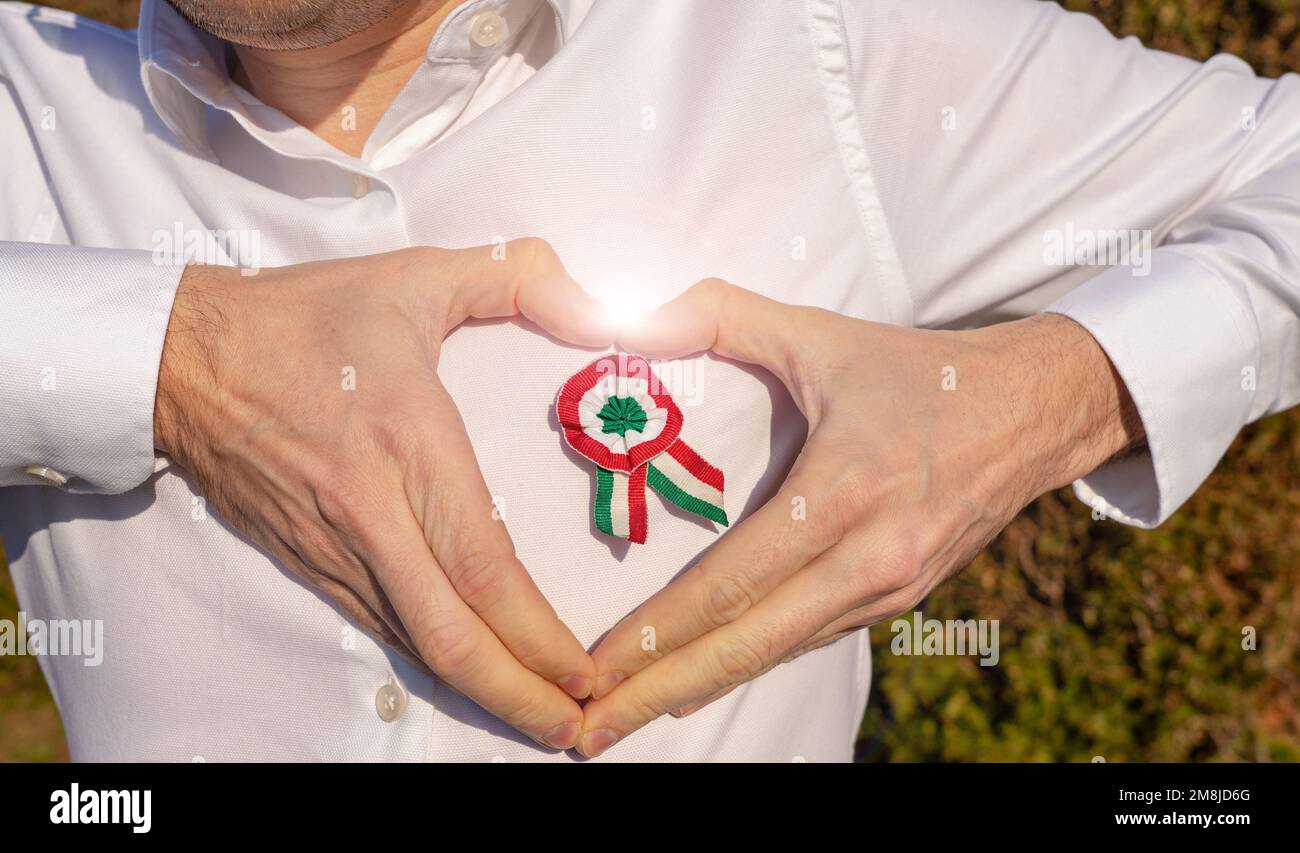 man plea a white shirt with tricolor rosette symbol of the hungarian national day 15th of march hands holidng in heart shaped round the rosette with Stock Photo