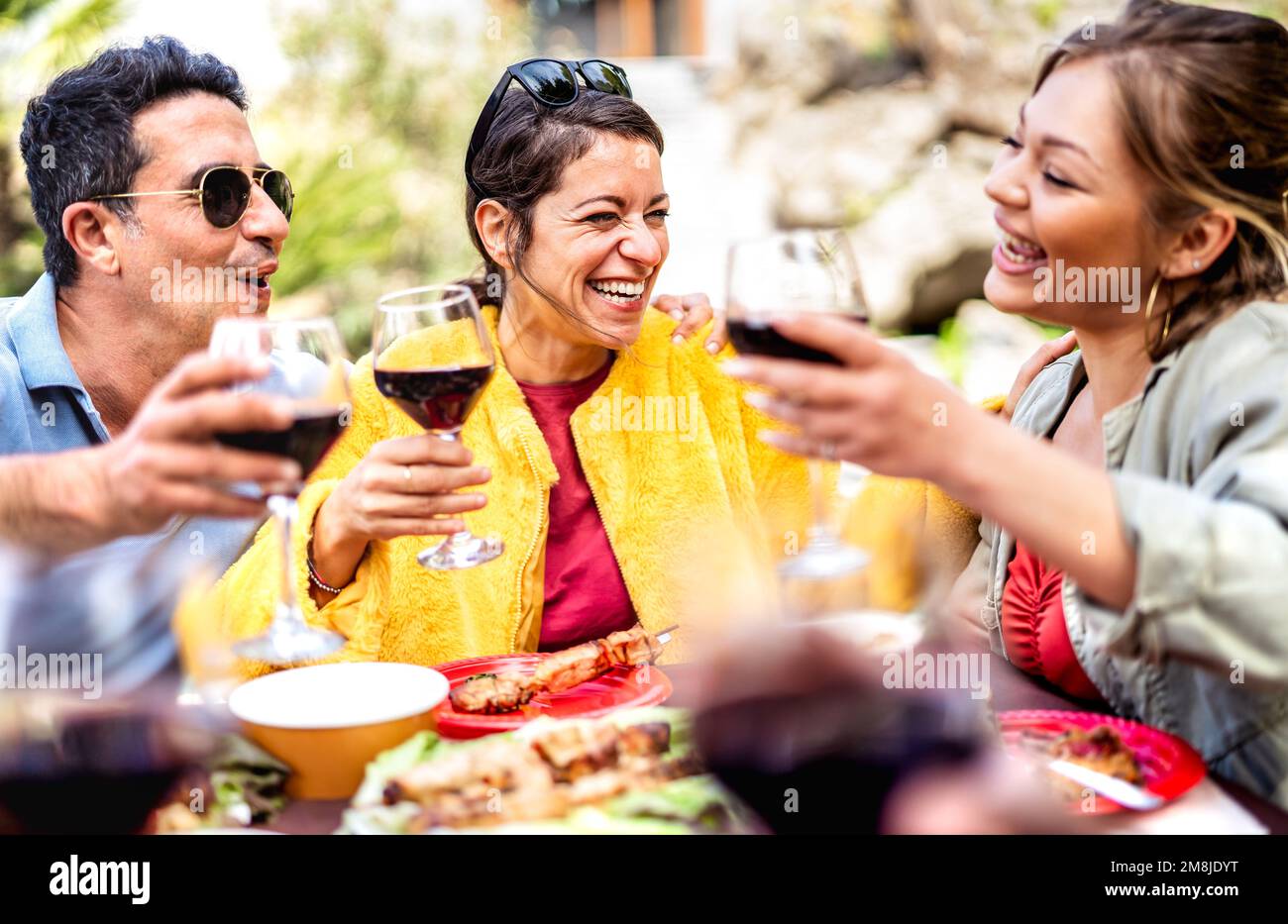Happy friends on genuine mood drinking red wine at pic nic party - Mixed age range people having fun together at restaurant winery patio out side Stock Photo