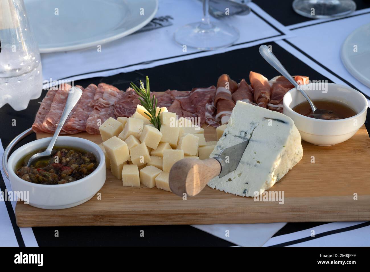 Assortment of cheese and processed meats on a wooden plate in a restaurant setting outdoors illuminated with natural light, realistic composition in a Stock Photo