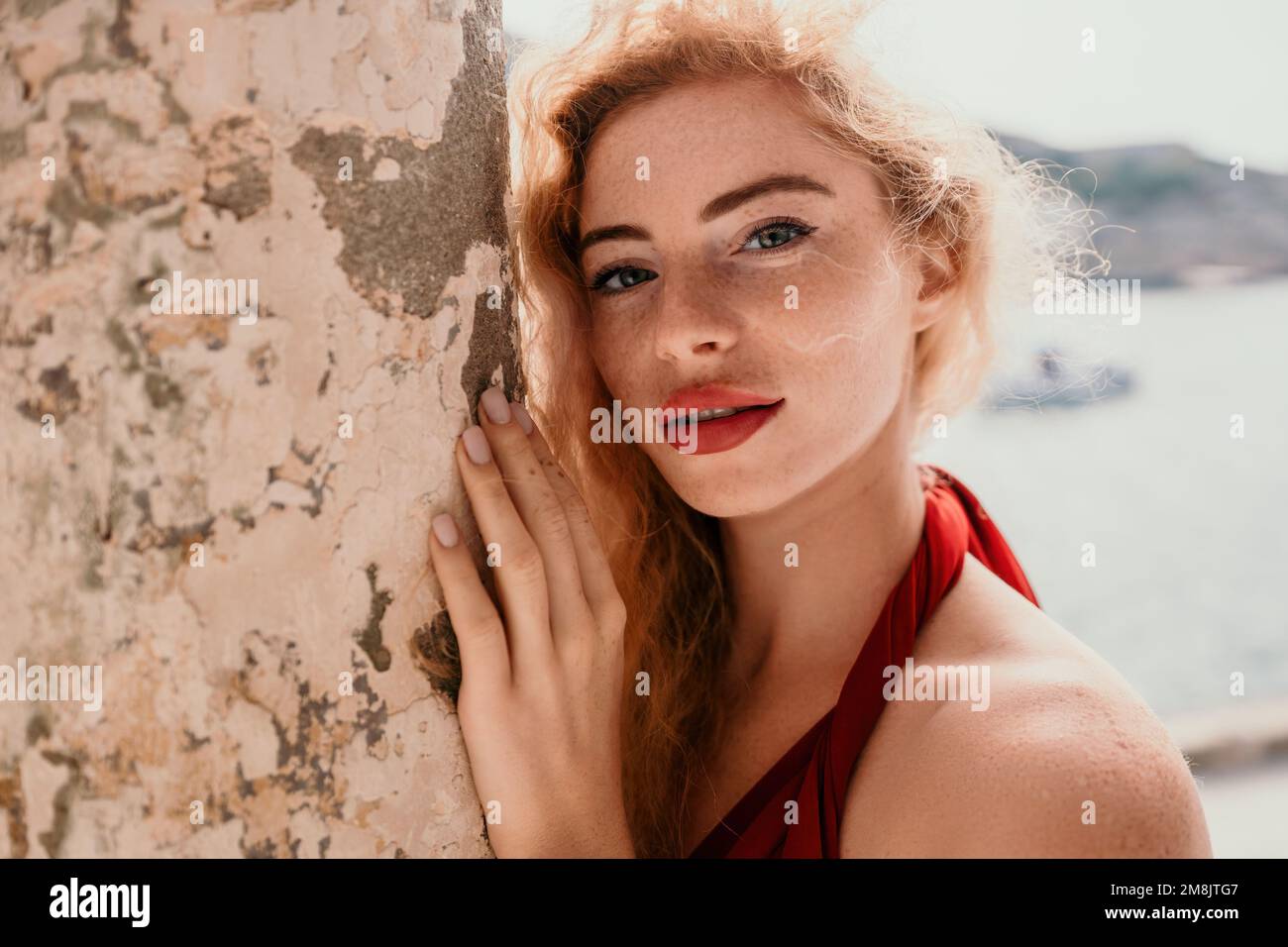 Redhead woman portrait. Curly redhead young caucasian woman with freckles looking at camera and smiling. Cute woman close up portrait in a red long Stock Photo