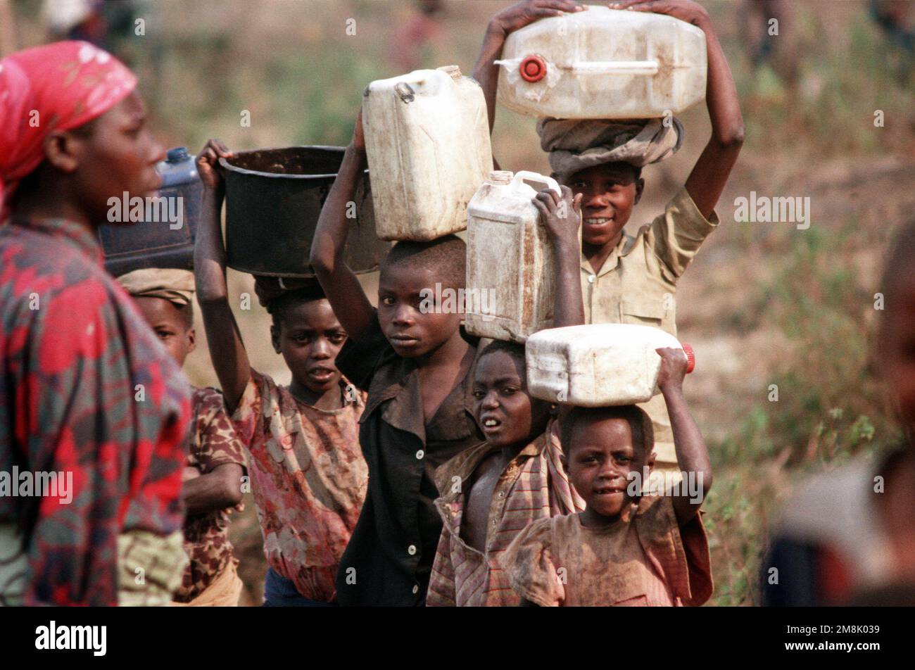 Children, displaced refugees from Rwanda's bitter civil war between the Hutus and Tutsis tribes in Southern Africa, carry containers of water atop their heads. From AIRMAN Magazine's December 1994 issue 'Front Cover' and issue 'Will You Please Pray for US?' -Relief for Rwandan Refugees. Country: Zaire (ZAR) Stock Photo