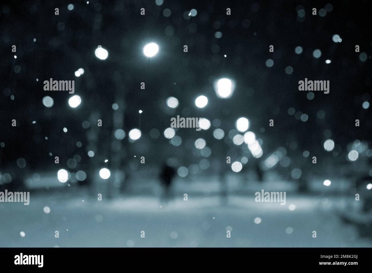 Blurred background. City view, lights, falling snow, night, street, bokeh spots. Urban backdrop winter scenery of street in city at night. Lantern light, snowfall. People. Blue color Stock Photo