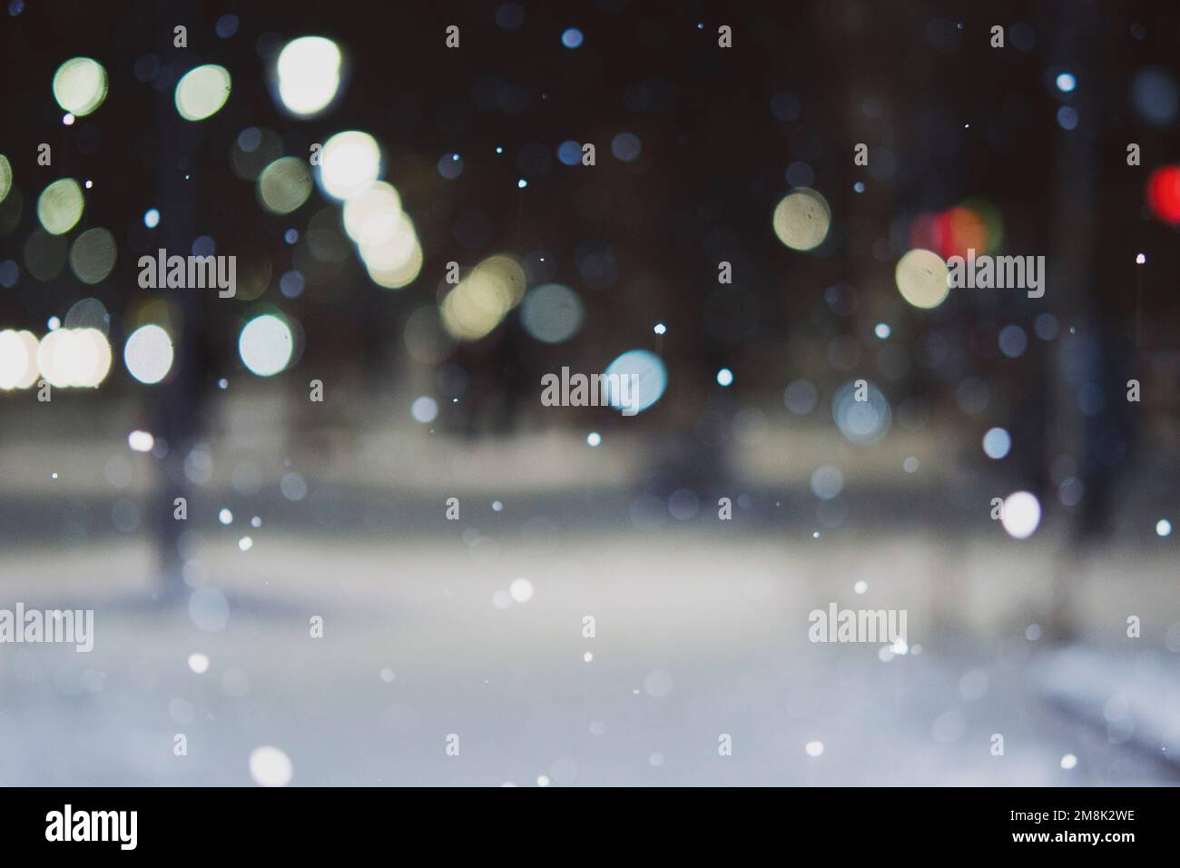 Blurred background. City view, lights, falling snow, night, street, bokeh spots of headlights of moving cars. Diffuse Urban backdrop winter scenery of street in city at night. Lantern light, snowfall Stock Photo