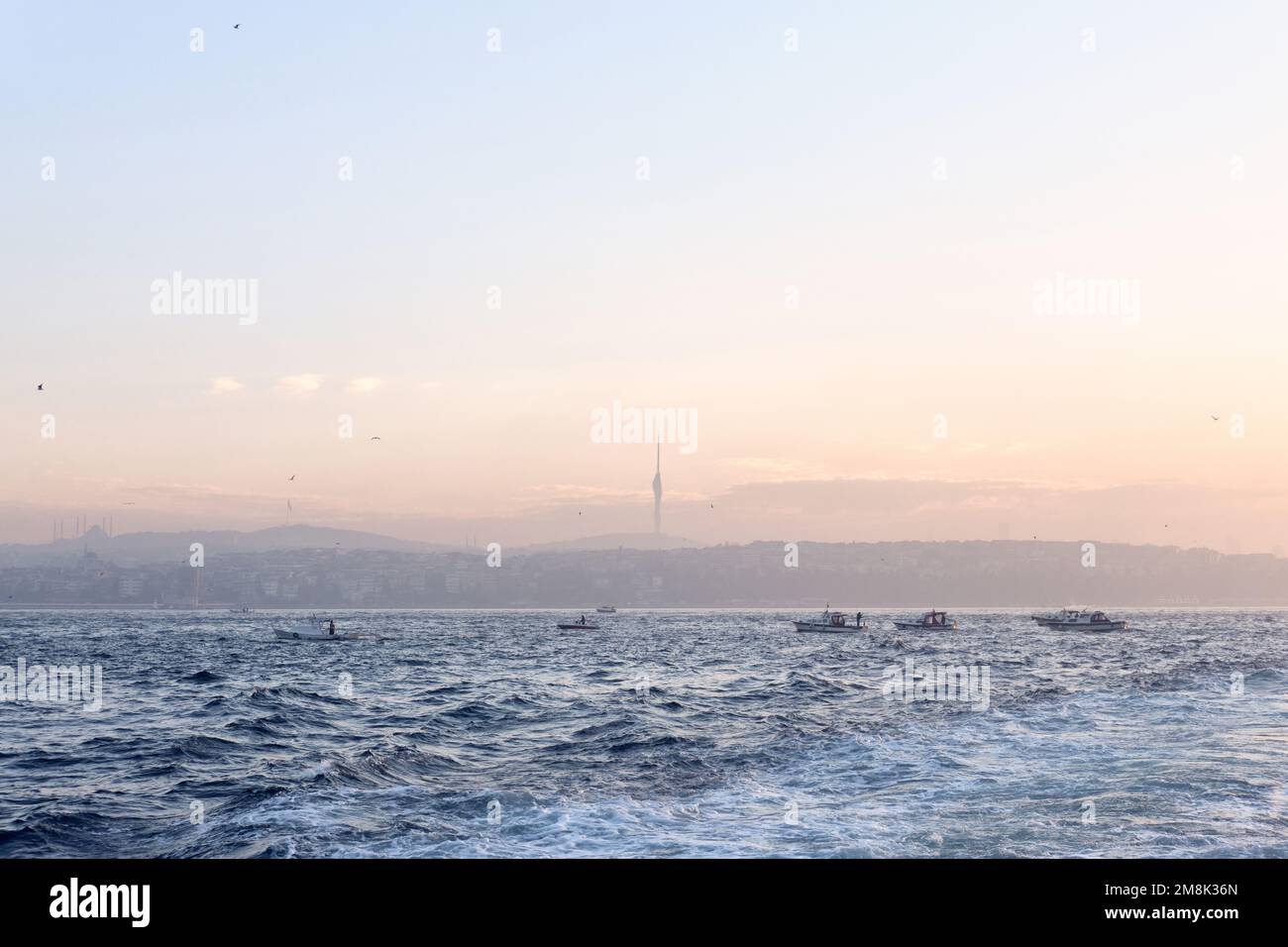 Istanbul, Turkey - January, 2023: Fisherman boats fishing on Bosphorus Marmara Sea when sunrise behind Anatolian side skyline with Camlica Tower Stock Photo
