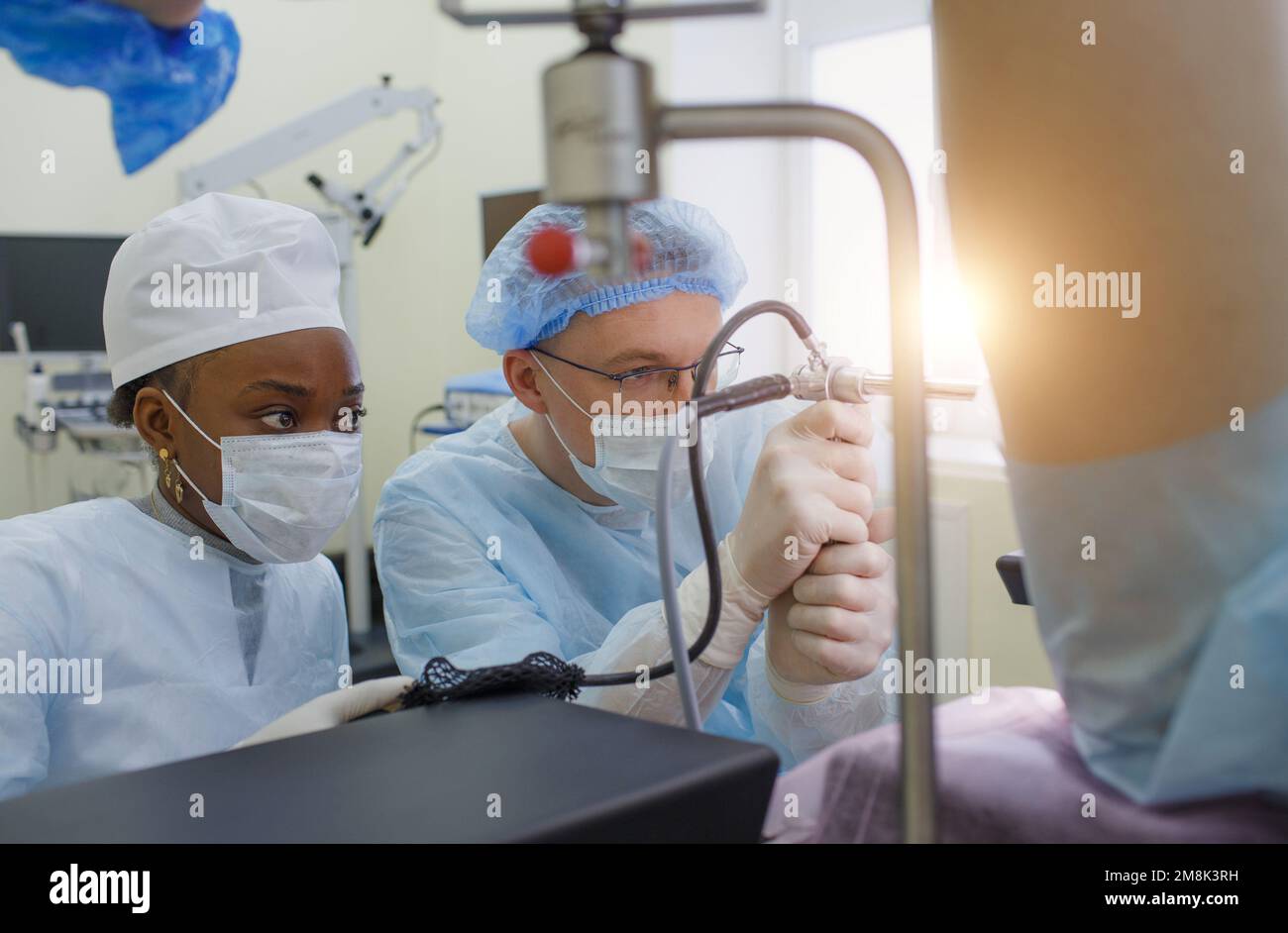 a proctologist with an assistant performs an operation on a patient lying on a proctological chair Stock Photo