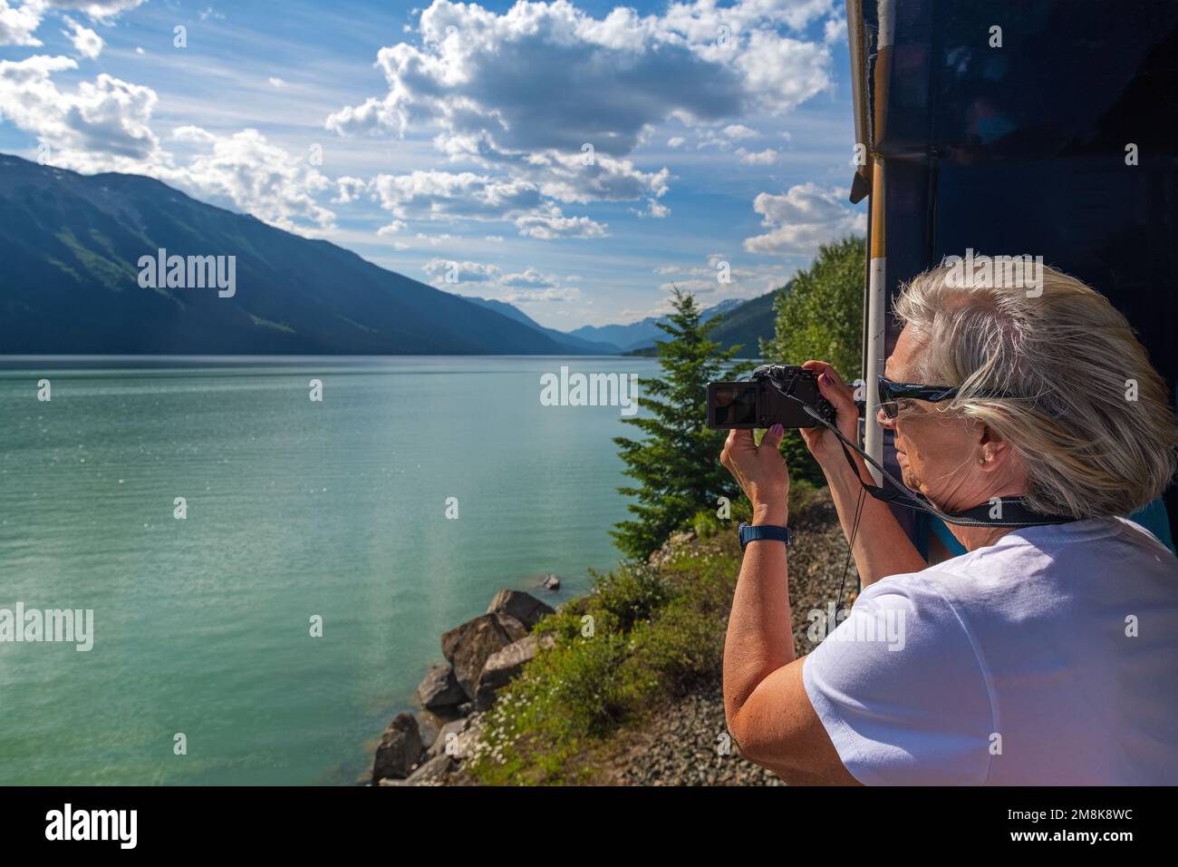 Female tourist taking photographs of Moose Lake in gold leaf wagon of Rocky Mountaineer train in Jasper national park, Canada. Stock Photo
