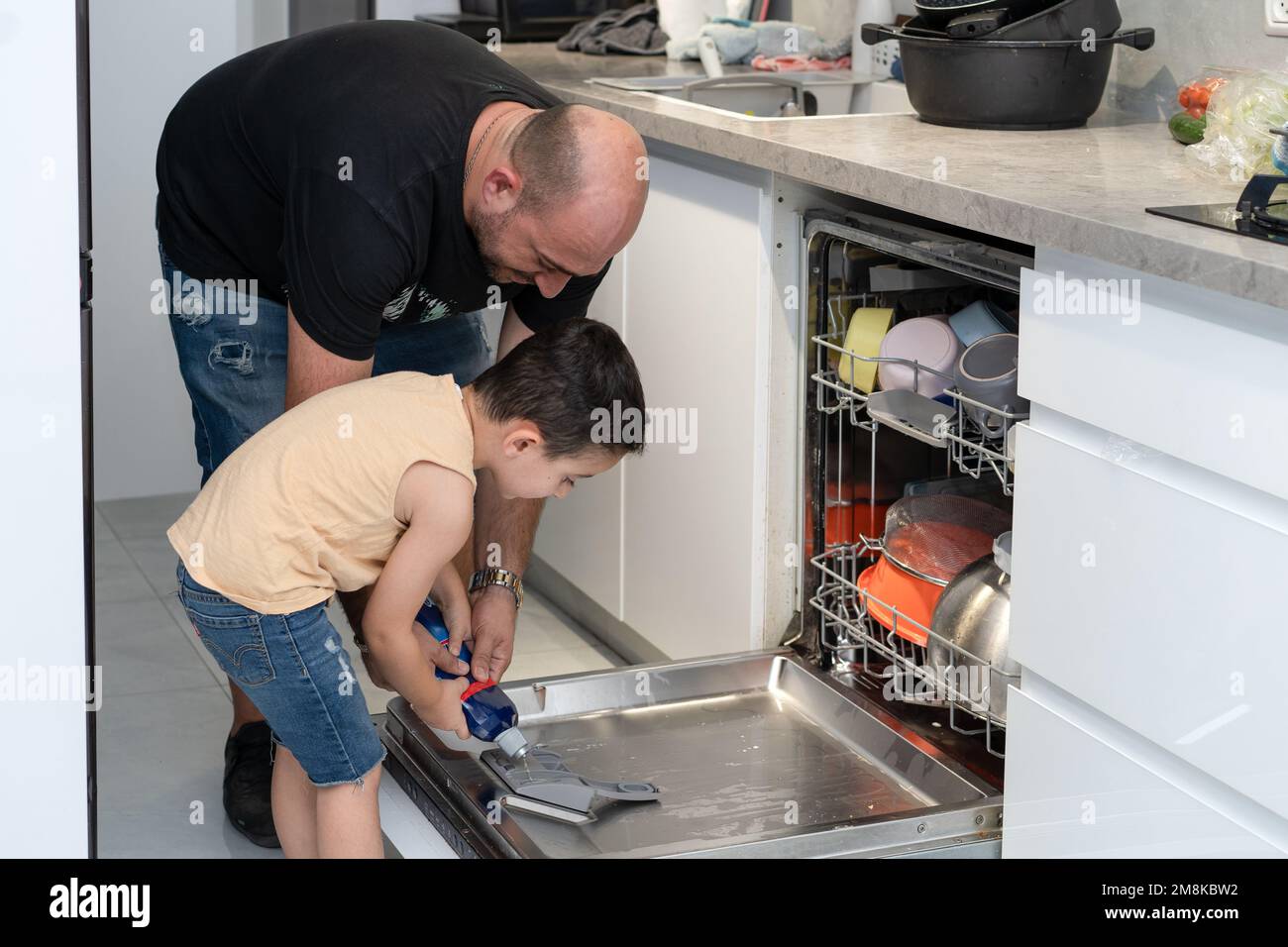 Father and son loading dishwasher together. Dad teach toddler son to
