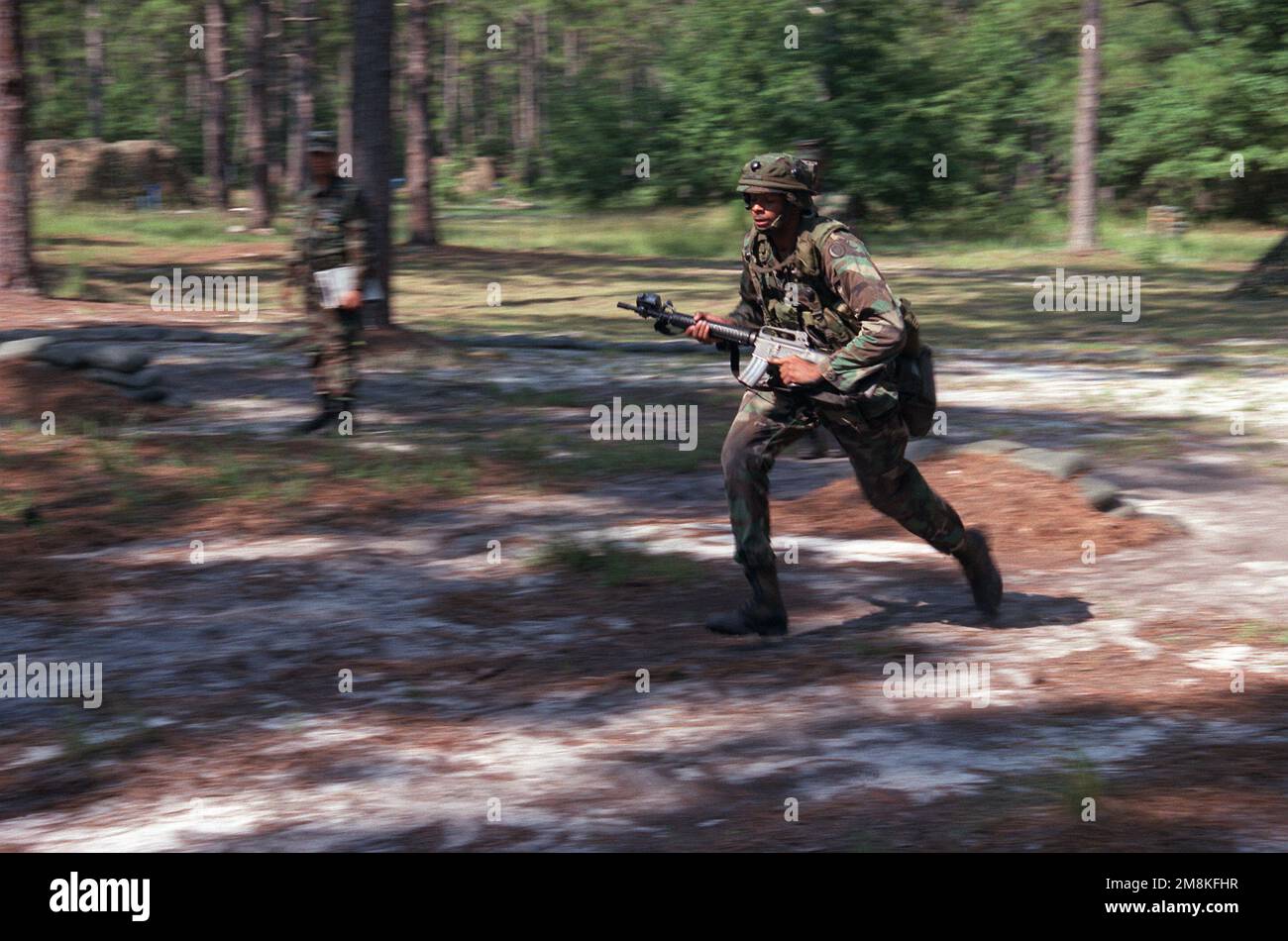 A soldier runs through the test area carrying an M16 rifle as an instructor looks on during Expert Infantry Badge (EIB) training. Base: Fort Stewart State: Georgia (GA) Country: United States Of America (USA) Stock Photo