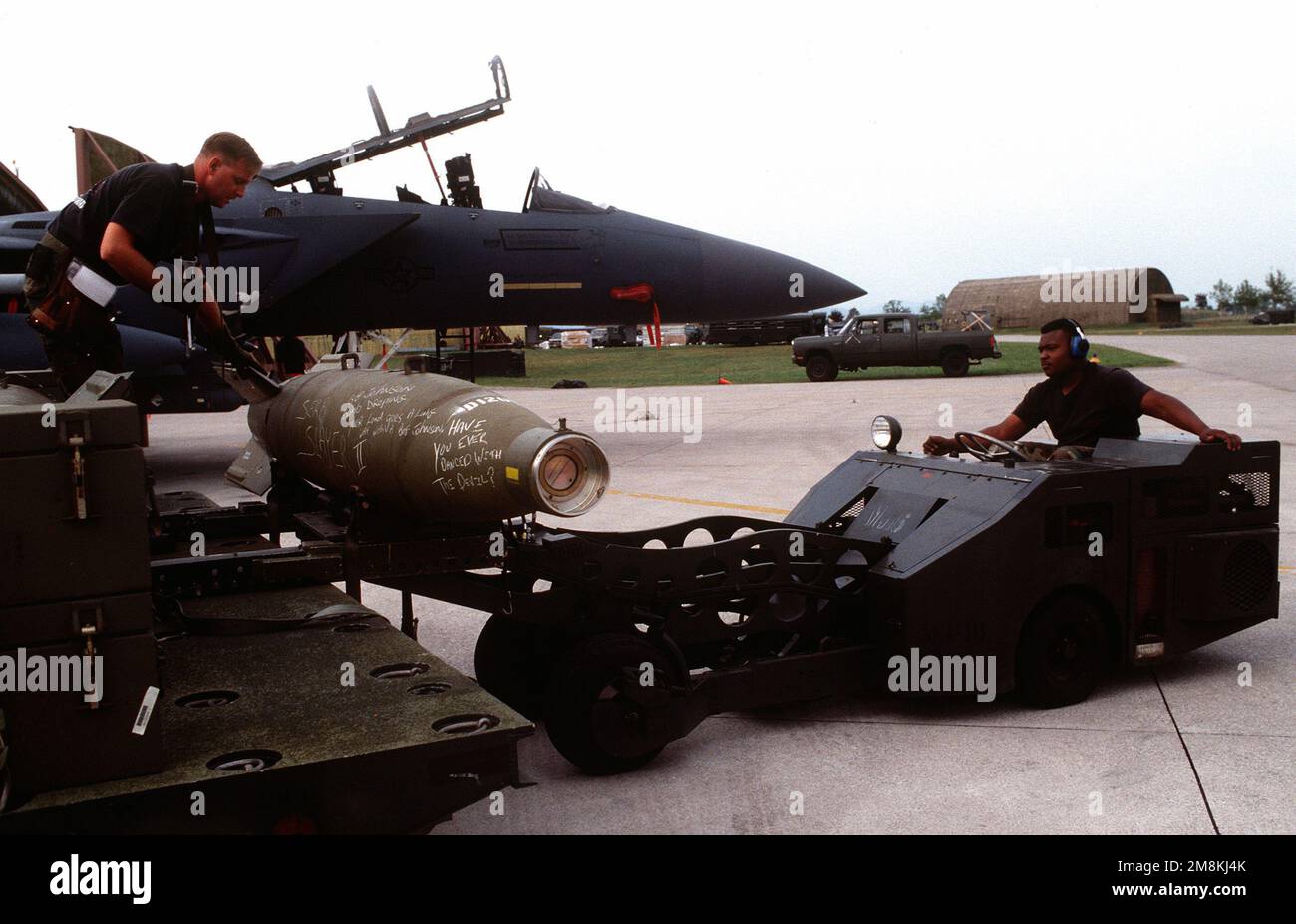 Weapon loaders offload the main body warhead and tail section of a laser guided bomb from a heavy expanded mobility ammunitions trailer prior to being loaded onto a US Air Force F-16C Fighting Falcon aircraft from the 555th Fighter Squadron for NATO airstrikes against the Bosnian Serbs. An F-15 is parked in the background. Subject Operation/Series: DELIBERATE FORCE Base: Aviano Air Base State: Pordenone Country: Italy (ITA) Stock Photo