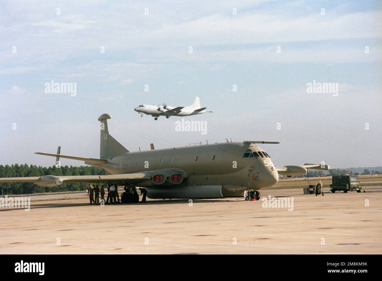 A United Kingdom Royal Navy Nimrod recon and patrol aircraft sits on the tarmac. The 120th CSX Squadron, RAF Kinloss, England maintains a four plane detachment at Jacksonville. In the background, a P-3C Orion aircraft is approaching for landing. Base: Naval Air Station, Jacksonville State: Florida (FL) Country: United States Of America (USA) Stock Photo