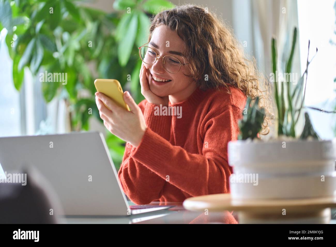 Young smiling woman holding smartphone using cellphone sitting at table. Stock Photo