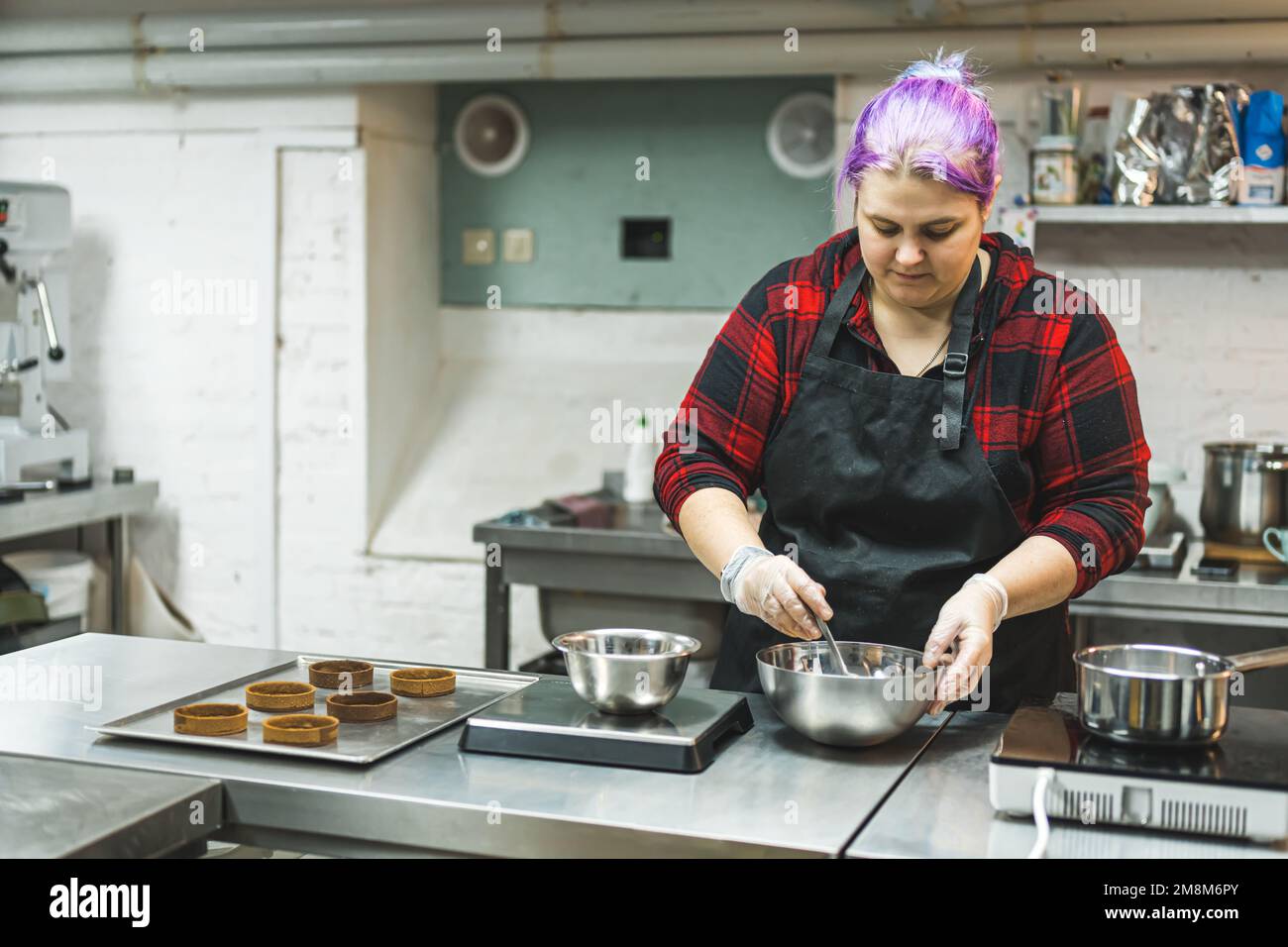 medium shot of a professional female chef with purple hair preparing caramel in a bowl in the kitchen. High quality photo Stock Photo