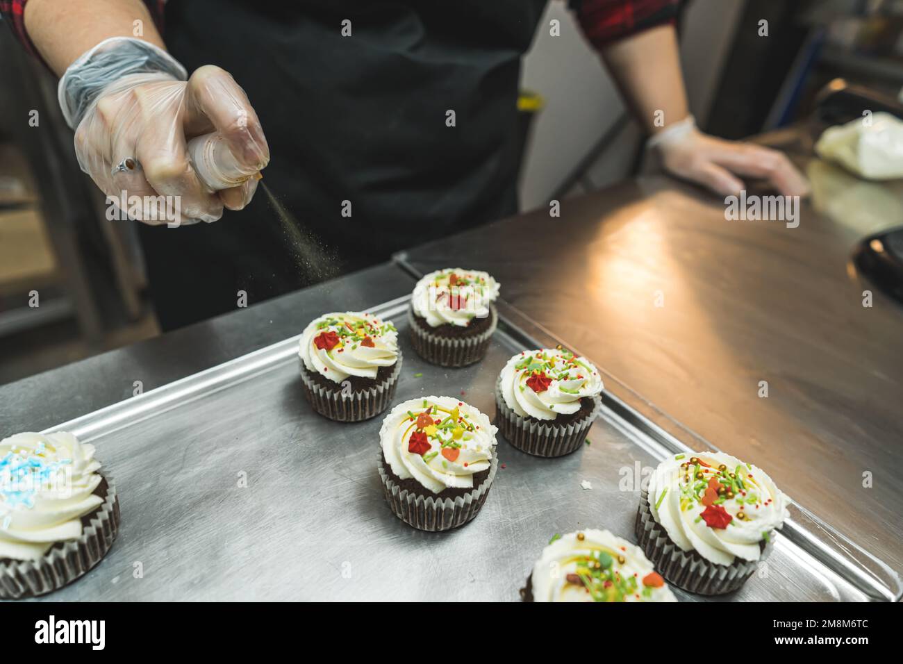 a baker adding sparkles for christmas cupcakes at the bakery, closeup view, holiday concept. High quality photo Stock Photo