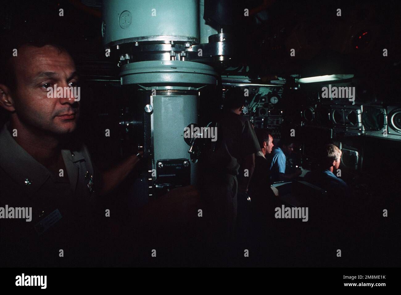 In this dimly lighted view of the interior of the nuclear-powered attack submarine USS Oklahoma City (SSN-723) control room, a Navy commander at the periscope and the bow plane control personnel at their stations have a mystic appearance reflective of the submarine reputation of stealth. Country: Atlantic Ocean (AOC) Stock Photo