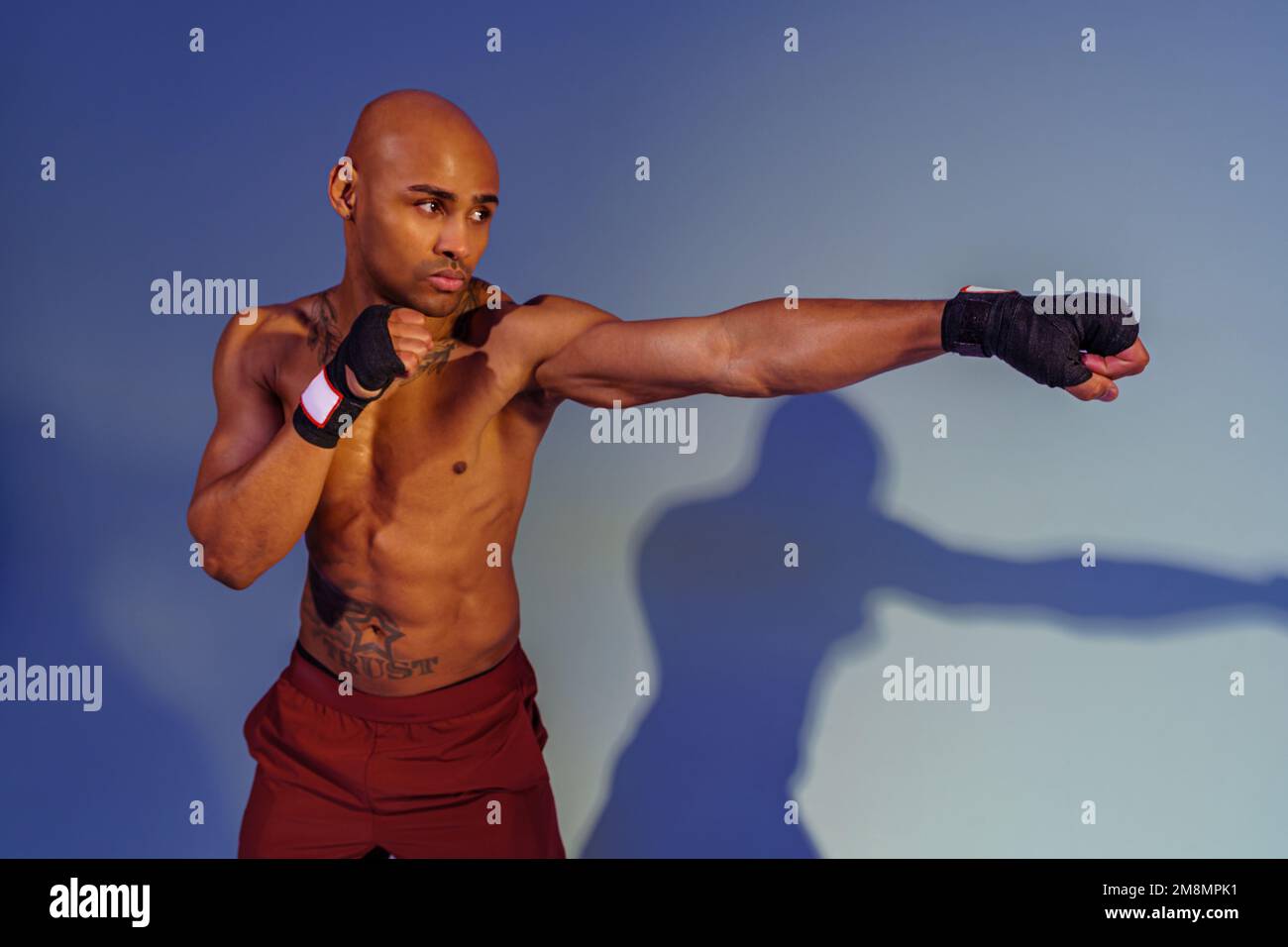 Professional kickboxer is training and practicing punch on studio background with shadows Stock Photo