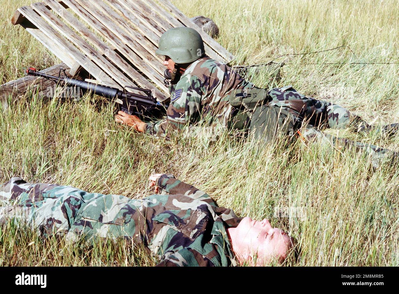 STAFF SGT. Scott Smith, 341st Medical Group, uses a field radio to report his position during an aggressor raid, while casualty STAFF SGT. Floyd Parrish, 341st Medical Group, lies nearby. For two days in late August 1997, the 341st Medical Group conducted a field deployment exercise with simulated attacks and casualties. Nearly two hundred Medical group personnel were deployed to an area that represented a small-scale air transportable hospital under constant threat of attack. The medical personnel were required to continue medical operations while maintaining their perimeter defense. Base: Ma Stock Photo