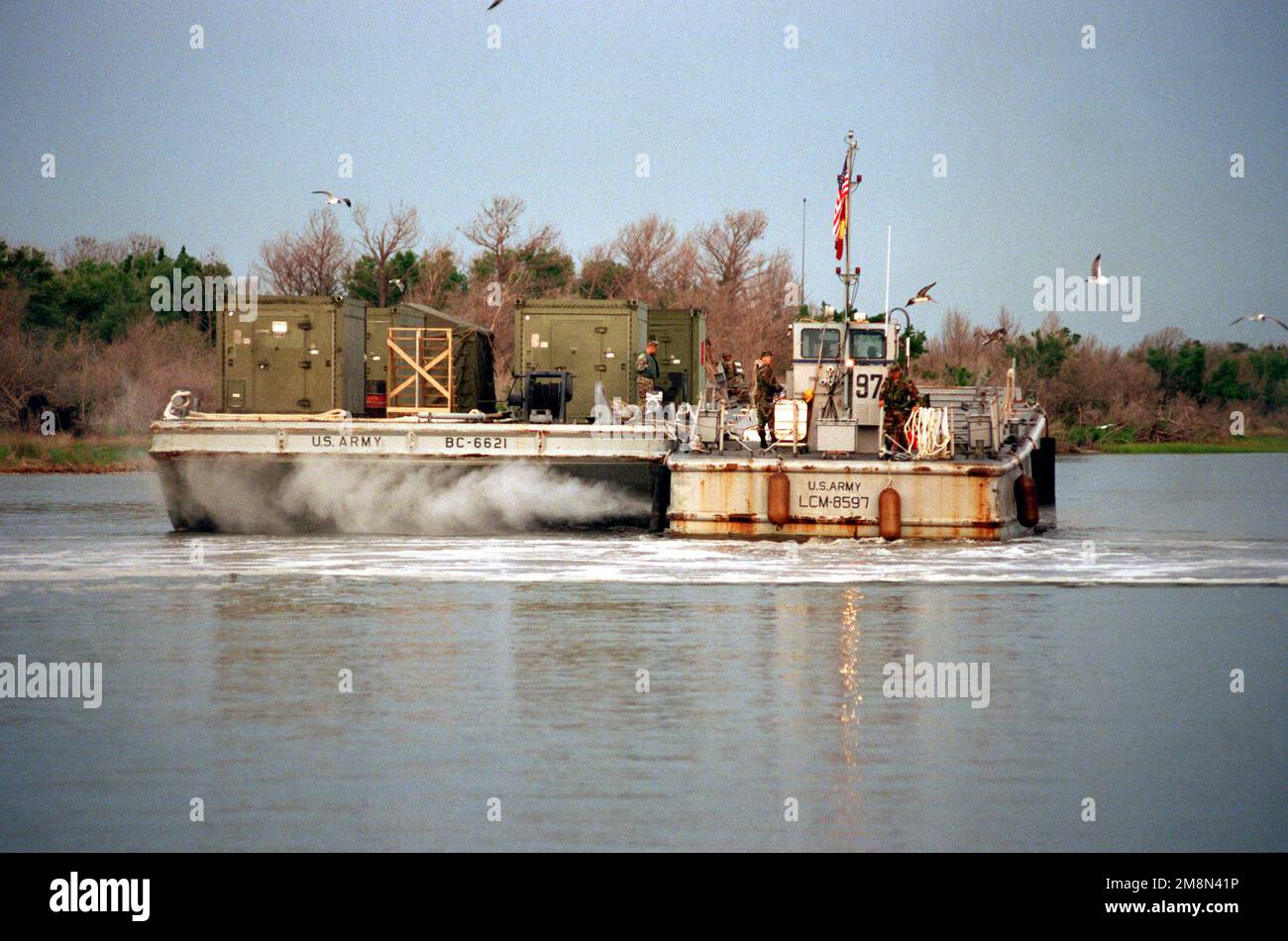 A US Army Landing Craft Mechanized (LCM) M-8 'Mike Boat,' tugs a cargo barge loaded with the Marine Corps' connex boxes containing maintenance and electrical equipment, en route from Mile Hammock Bay, New River, to the designated location where the Forward Support Base (FSB) is to be constructed along New River's Shoreline, at Camp Lejeune, North Carolina, in preparation for the Riverine Insertion Operation Exercise (RIOEX) '98. Subject Operation/Series: RIOEX '98 Base: Marine Corps Base, Camp Lejeune State: North Carolina (NC) Country: United States Of America (USA) Stock Photo