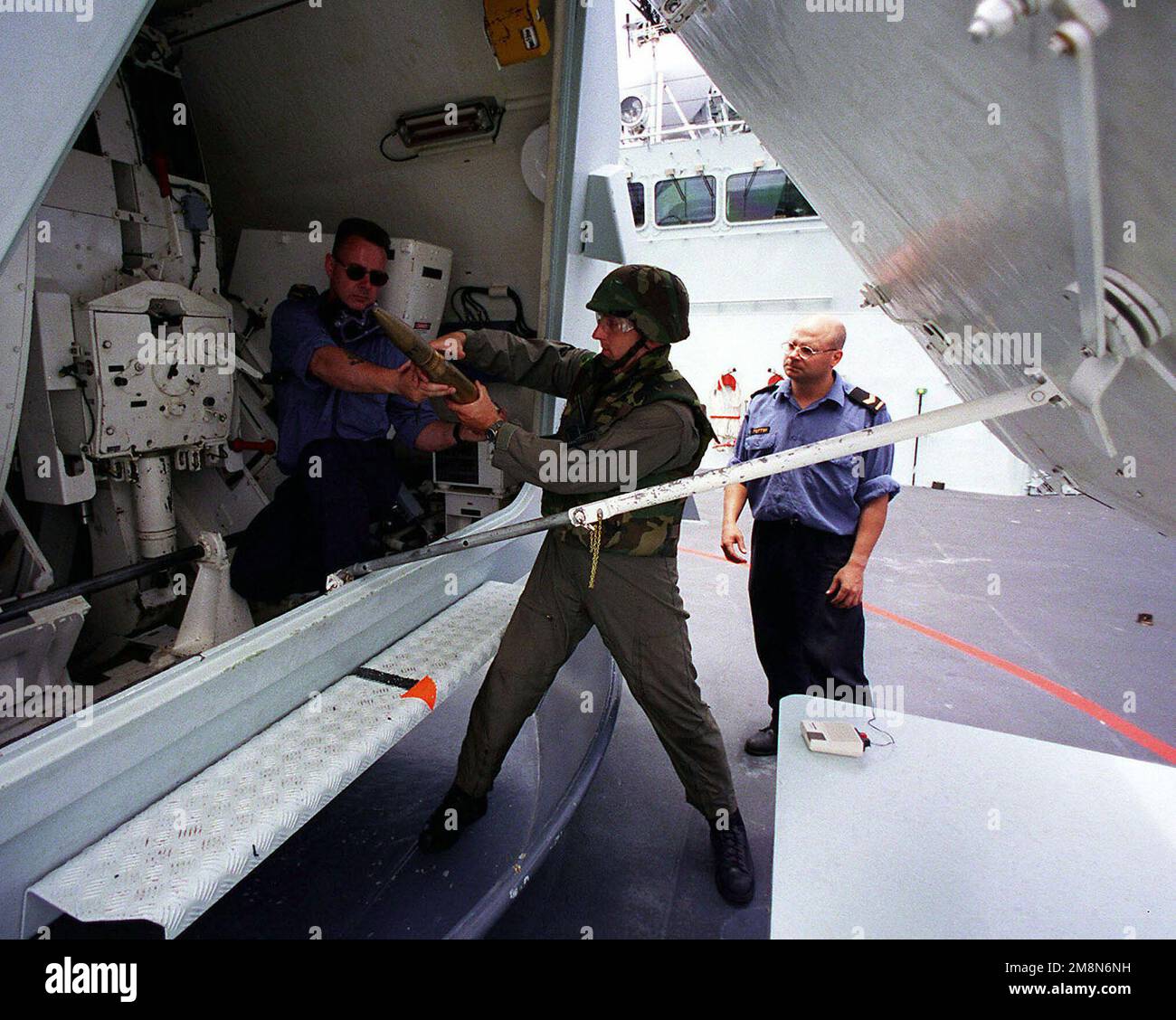 Leading SEAMAN Ken Sawyer (left), a weapons technician aboard the Canadian frigate HMCS REGINA, hands a shell from a jammed 57mm gun mount to PO1 Shelby Cornelius (center), Explosive Ordnance Disposal Mobile Unit Two from Whidbey Island, Washington, during the exercise RIMPAC 98. Another Canadian sailor looks on as the mount is unjammed. Leading Seaman Ken Sawyer (left), a weapons technician aboard the Canadian frigate HMCS REGINA, hands a shell from a jammed 57mm gun mount to PO1 Shelby Cornelius (center), Explosive Ordnance Disposal Mobile Unit Two from Whidbey Island, Washington, during the Stock Photo