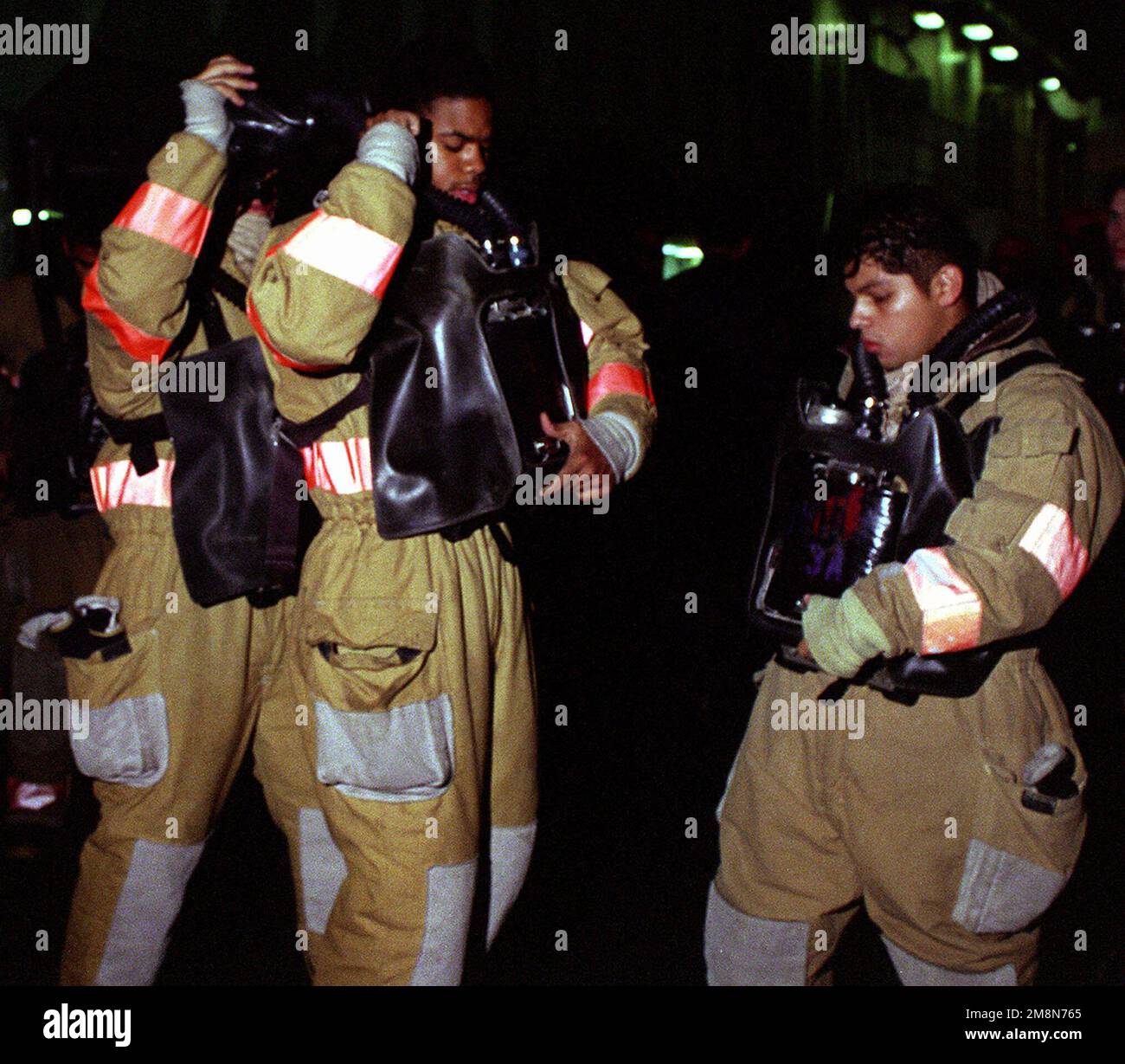 Fire party members aboard the auxiliary command ship USS CORONADO (AGF 11) assist one another in suiting up to fight a simulated fire during a general quarters drill as part of exercise RIMPAC 98. Subject Operation/Series: RIMPAC '98 Country: Pacific Ocean (POC) Stock Photo