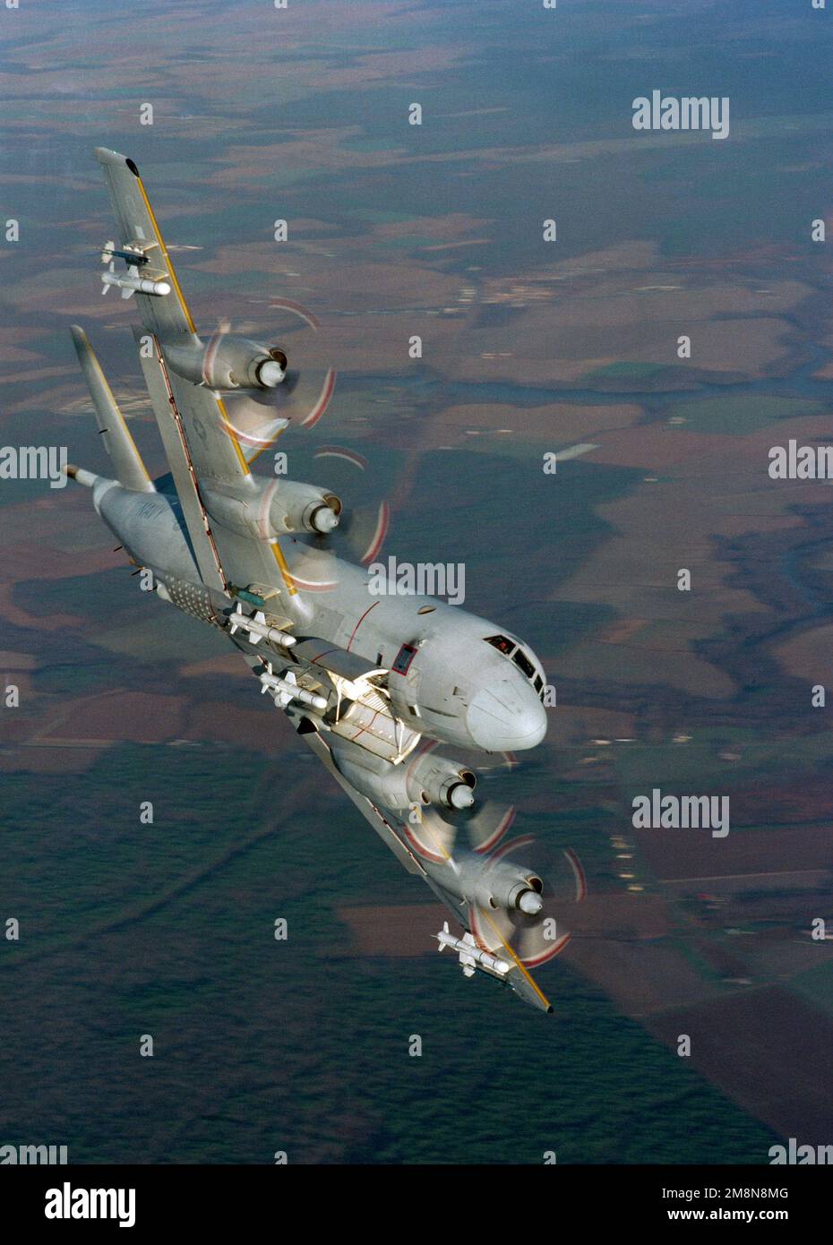 An air-to-air view of a P-3 Orion aircraft banking to the right. This aircraft is carrying an AIM-9 Sidewinder missile on each outboard wing pylon and a total of four Harpoon missiles under its wings and fuselage. Country: Unknown Stock Photo