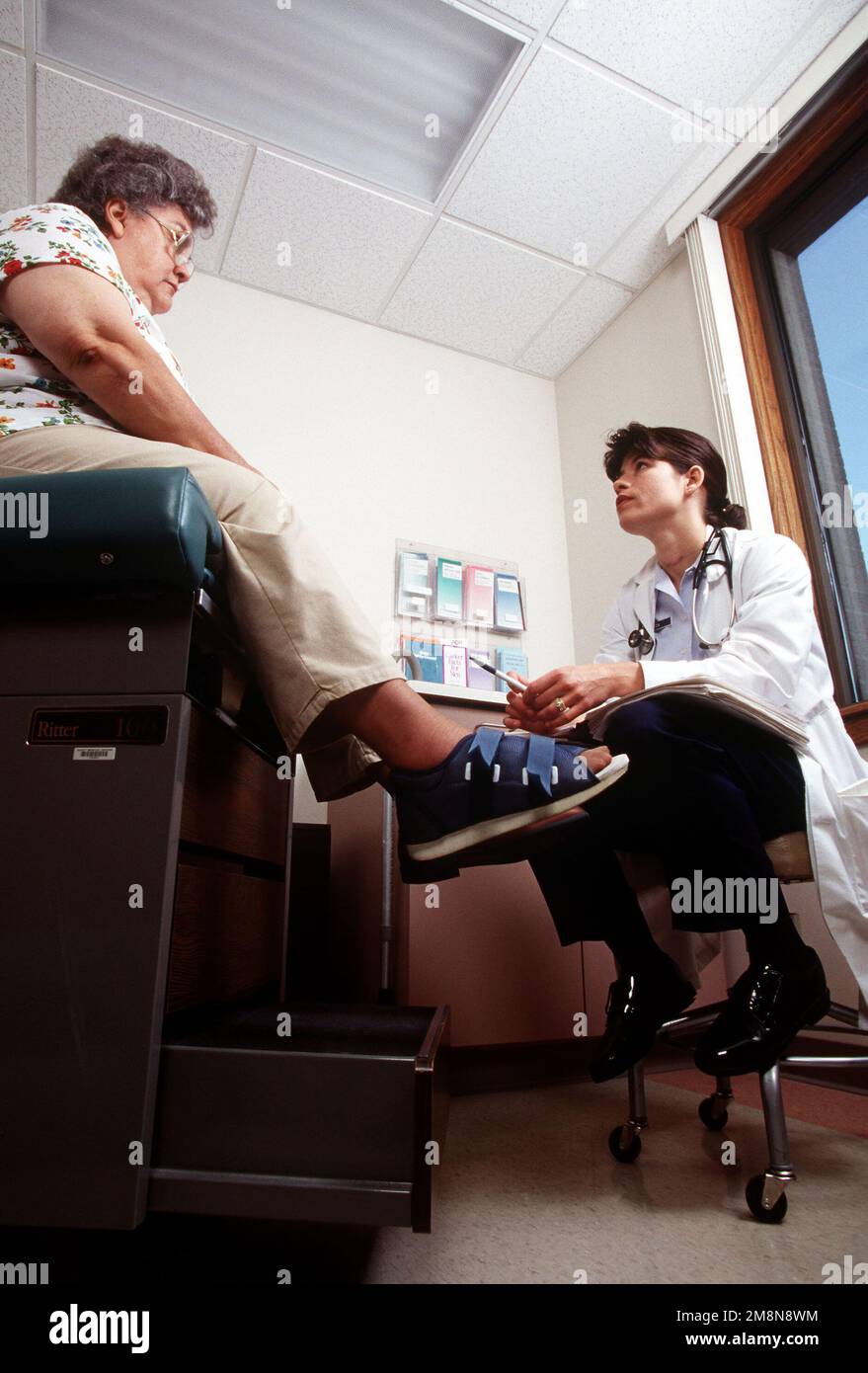 Left side front view from a low angle up at USAF Captain (Dr.) Melia Cox as she examines Darlene Schengel's foot before referring her to a specialist. Family practice physicians are one of the linchpins in the military's managed health care program called TRICARE. This image is seen in the September 1998 edition of AIRMAN Magazine. Base: Scott Air Force Base State: Illinois (IL) Country: United States Of America (USA) Stock Photo