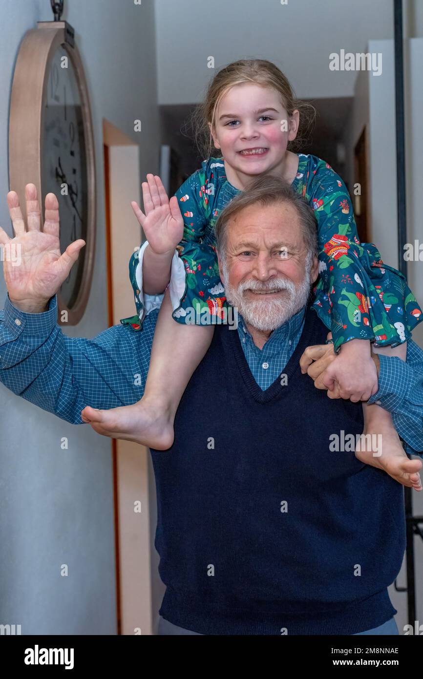 Grandfather having fun giving his six year old granddaughter a piggyback ride inside a hallway. (MR) Stock Photo