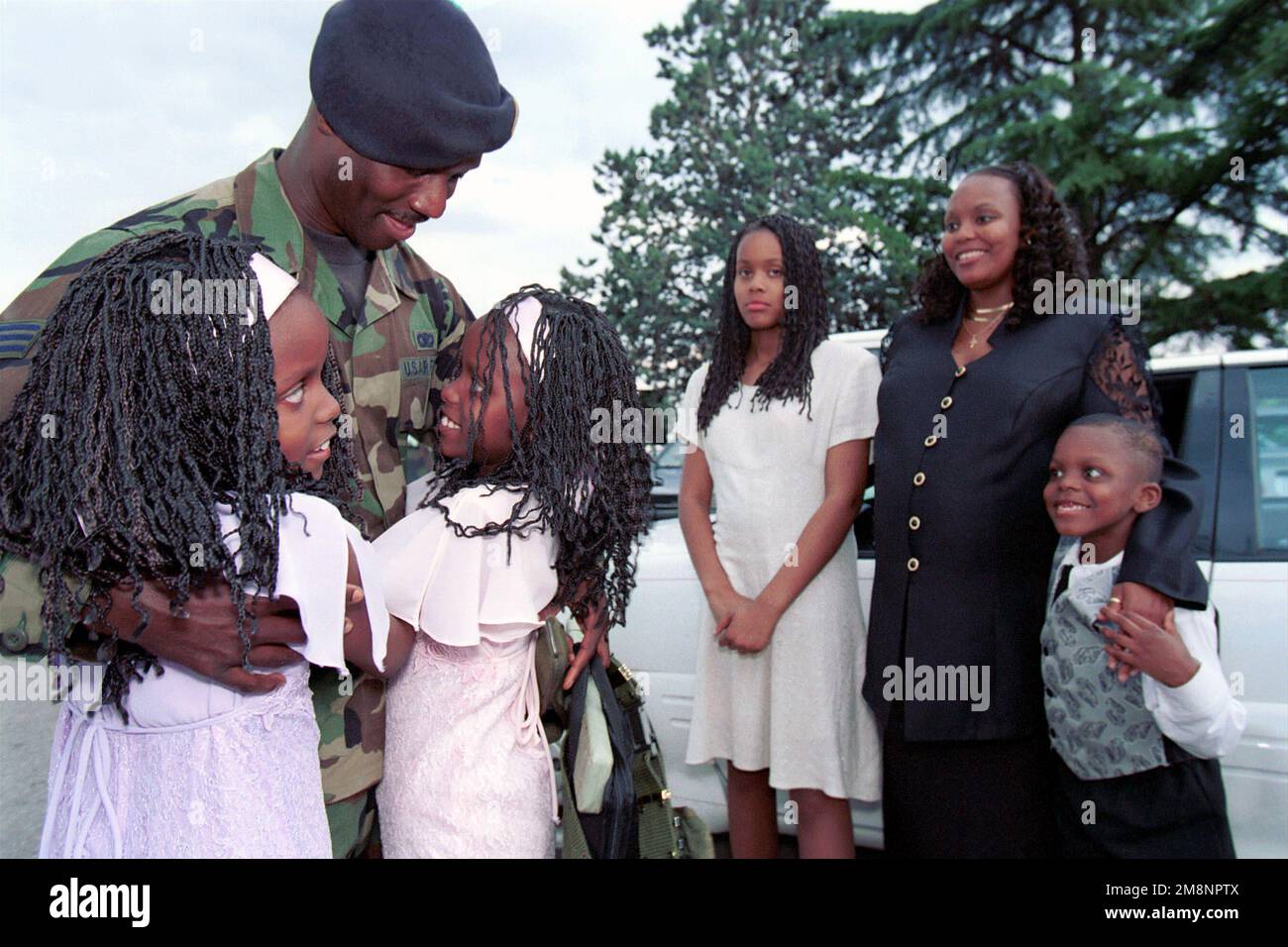 SENIOR AIRMAN Jerome Mack, a 31st Security Forces Squadron Patrolman and Desk Sergeant, hugs his twin daughters, Antona and Antoinette. His daughter Shaccara; wife, Pat; and son, Anthony, are in the background. This photograph is part of the story in the July, 1999 AIRMAN Magazine article 'Fighting the War from 'Home'. Subject Operation/Series: ALLIED FORCE Base: Aviano Air Base State: Pordenone Country: Italy (ITA) Stock Photo