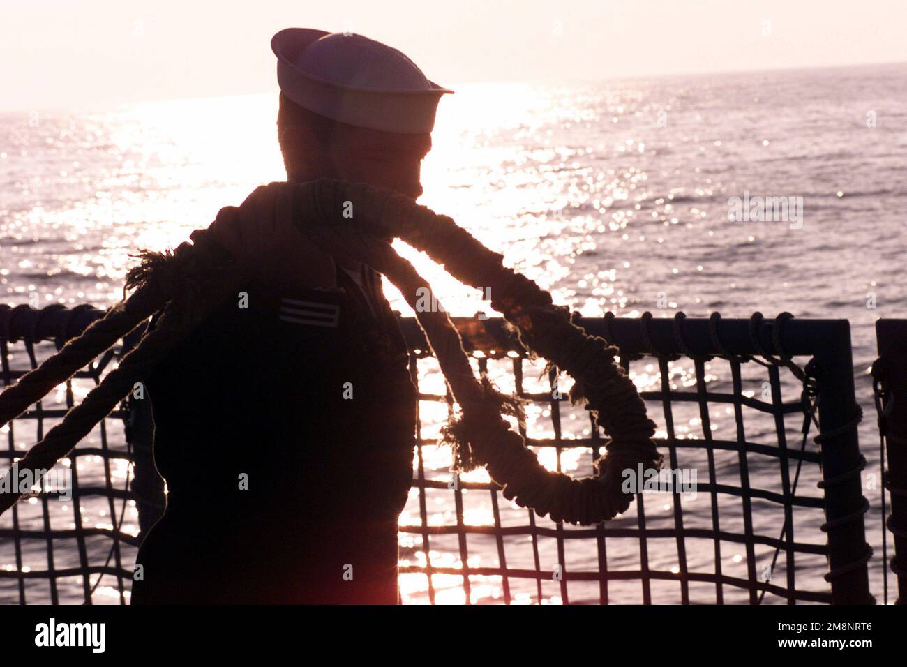 The evening sun sets behind a sailor tending lines during sea-and-anchor detail aboard USS REUBEN JAMES (FFG 57) as the ship pulls in to Antofagasta, Chile, while participating in Exercise TEAMWORK SOUTH '99. Subject Operation/Series: TEAMWORK SOUTH '99 Base: USS Reuben James (FFG 57) Stock Photo