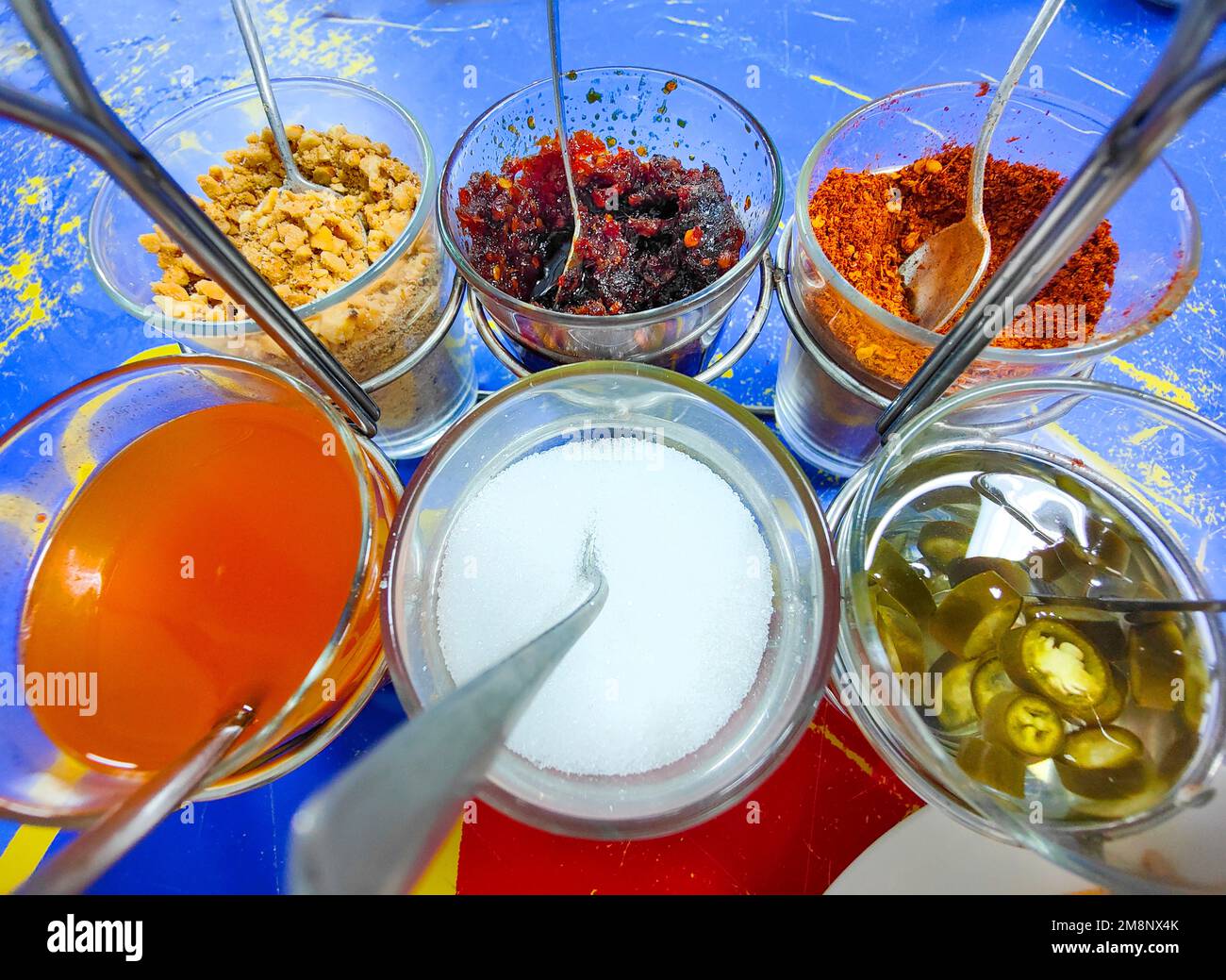 Glass bowls containing ground peanuts,sweet chilli paste,pickled chilli,sweet sauce,sugar and chilli flakes,to sprinkle on your food. Stock Photo