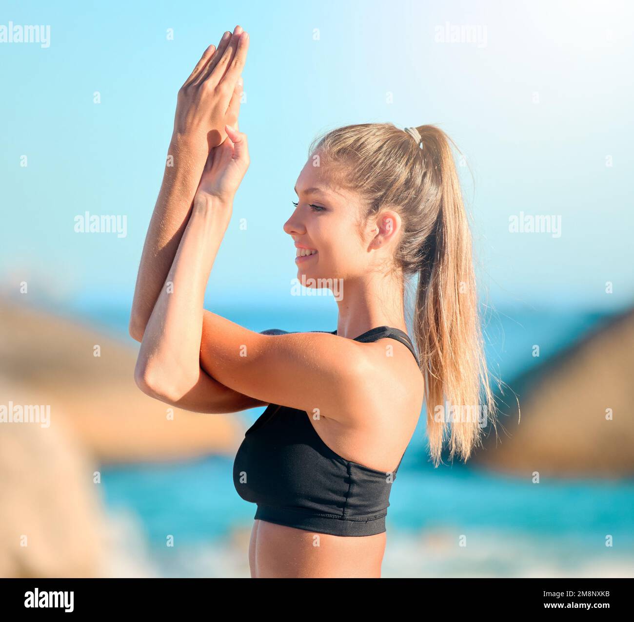 Beautiful woman practising yoga exercise on the beach. Young female athlete stretching while working out outside. Finding inner peace, balance and Stock Photo