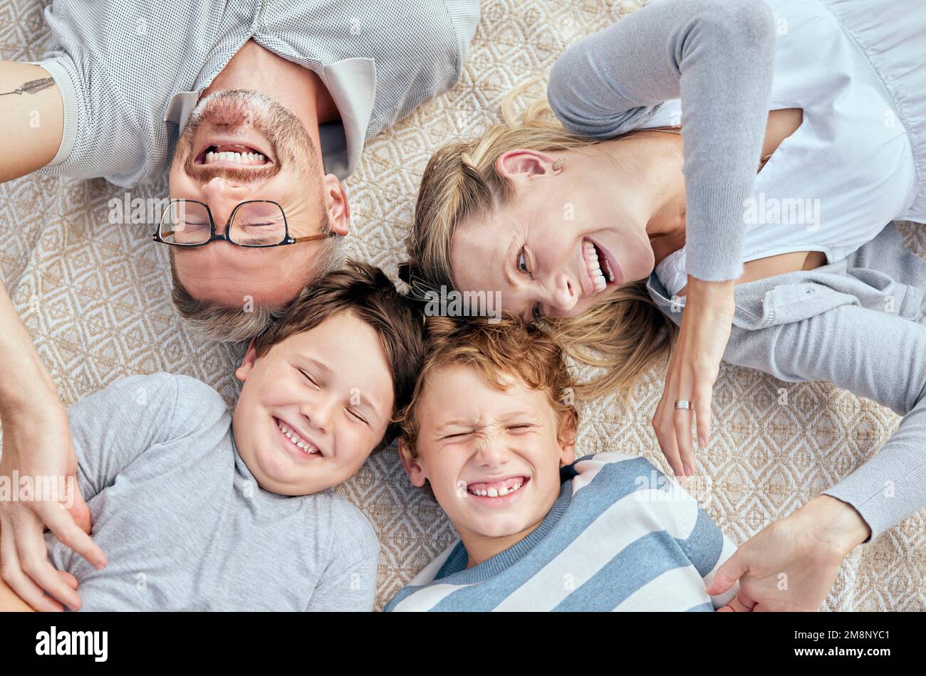 Carefree loving parents from above tickling and teasing their cute little laughing sons. Happy caucasian family of four relaxing and playing together Stock Photo