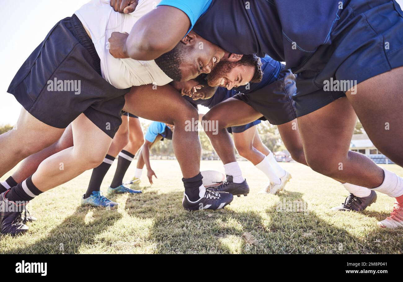 Below two opponent rugby teams contesting a scrum during a match outside on a field. Rugby players battling and fighting to win the ball while Stock Photo