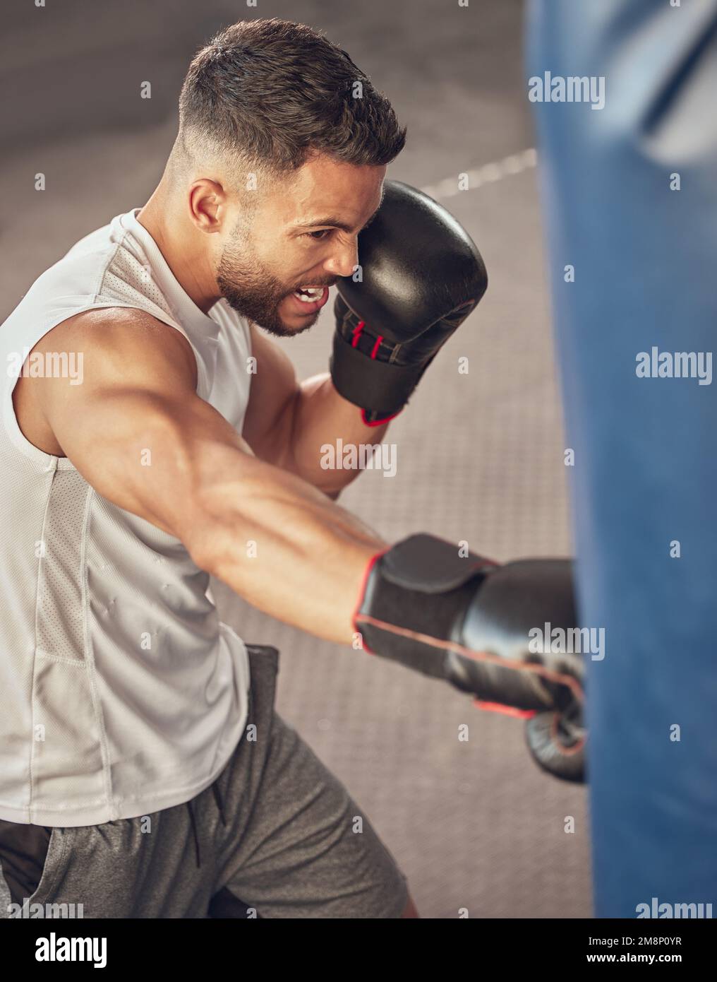 Strong boxer hitting punching bag. Mma fighter wearing boxing gloves in combat training. Bodybuilder doing cardio training in the gym. Active boxer Stock Photo