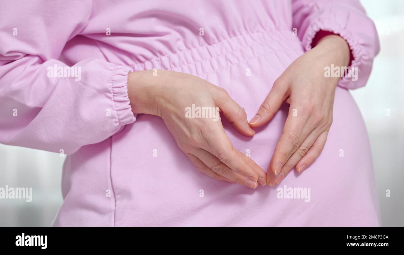 Pregnant woman shows fingers heart near big bump with baby Stock Photo