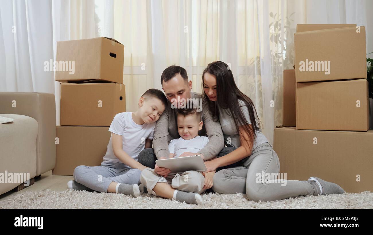 Excited family sits among boxes on floor and looks at tablet Stock Photo
