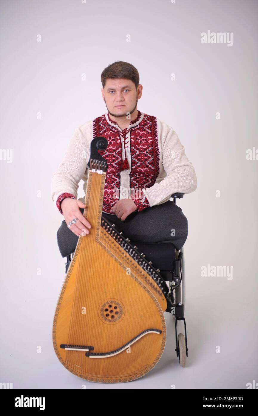 handsome young man with kobza musical instrument in hands sits on white background war veteran dressed in Ukrainian embroidered shirt national symbols Stock Photo