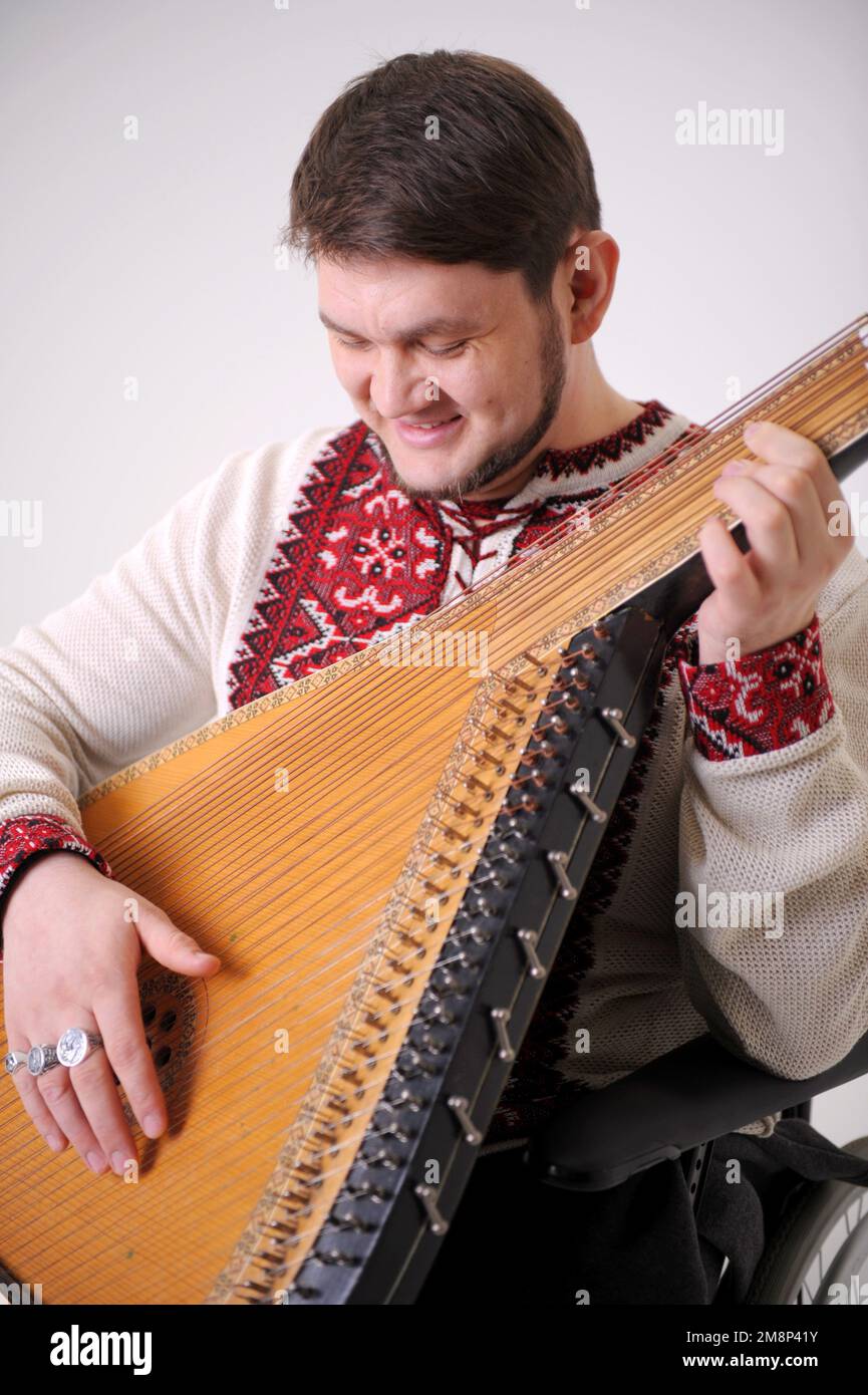young handsome male Cossack of Ukraine plays the harp and smiles the musician holds the kobza and looks at 30 years old white and red embroidered shir Stock Photo