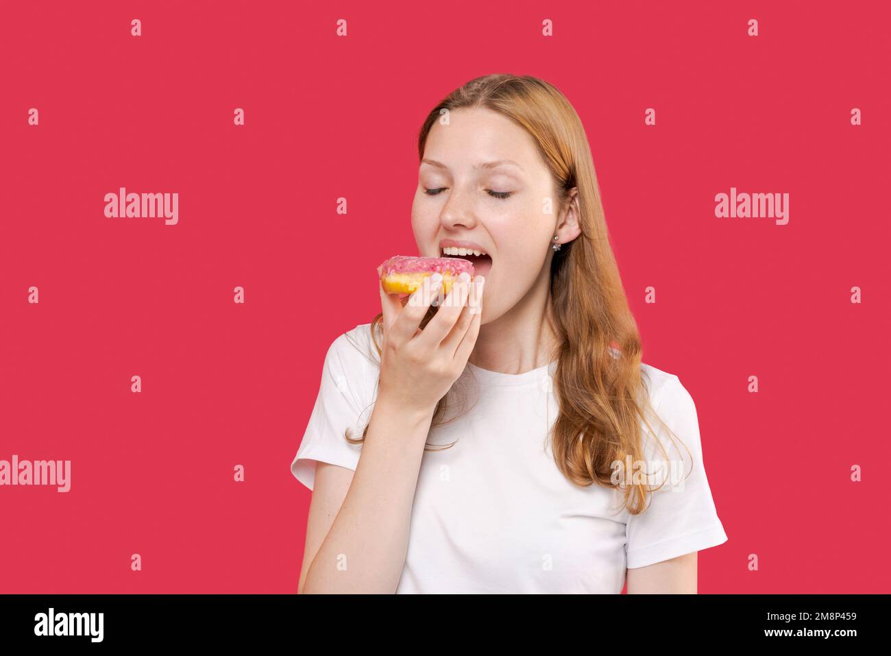 Young woman having fun and eating junk food sweet donut, wearing white ...