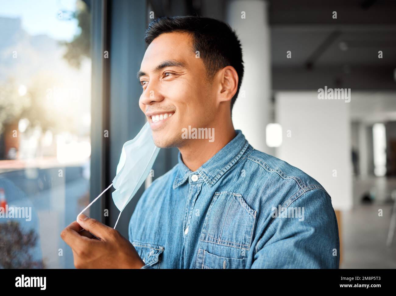 Young cheerful asian businessman removing his mask while at work. One