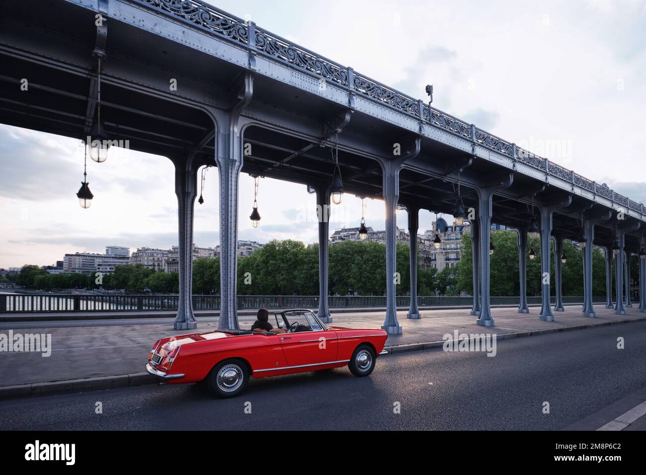 Paris, France - May, 2022: A red clasical sport car with long steel columns of Passy Viaduct located at Pont de Bir Hakeim Bridge Stock Photo