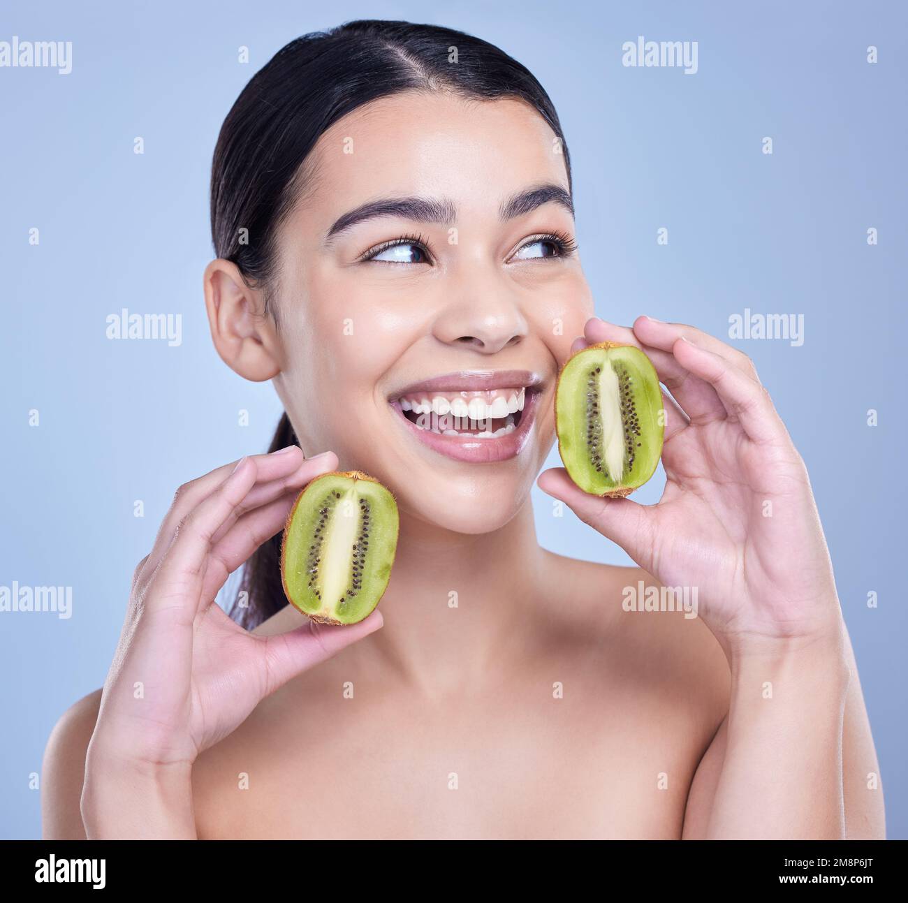 A happy smiling mixed race woman holding a kiwi fruit. Hispanic model promoting the skin benefits of a healthy diet against a blue copyspace Stock Photo