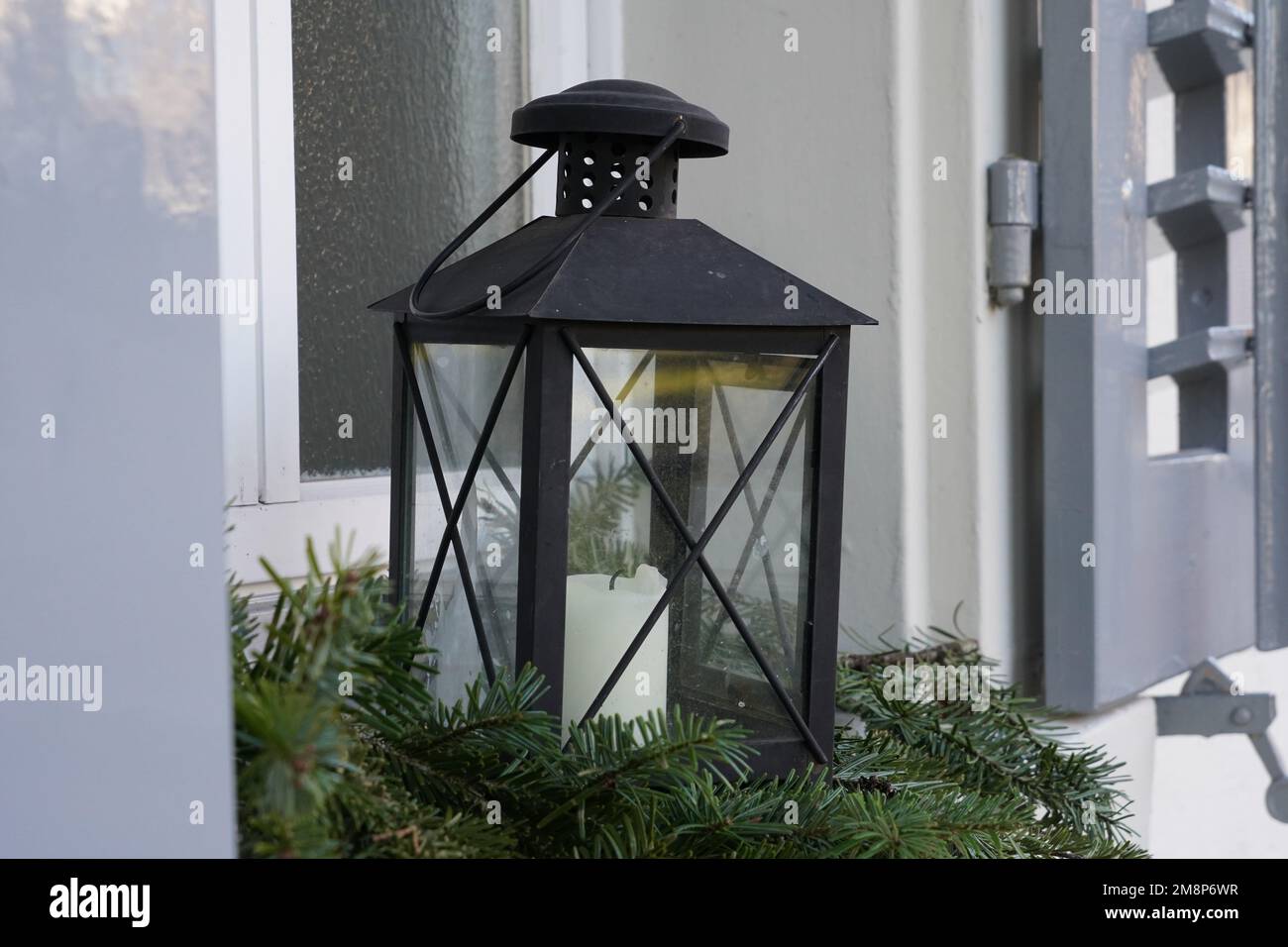 A lantern with a candle is arranged on a windowsill on coniferous twigs. Stock Photo