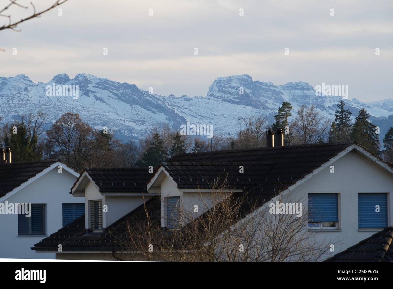 Rooftops of residential quarter in a Swiss town Hinwil  surrounded with Alp mountains. The mountains are covered with snow. Stock Photo